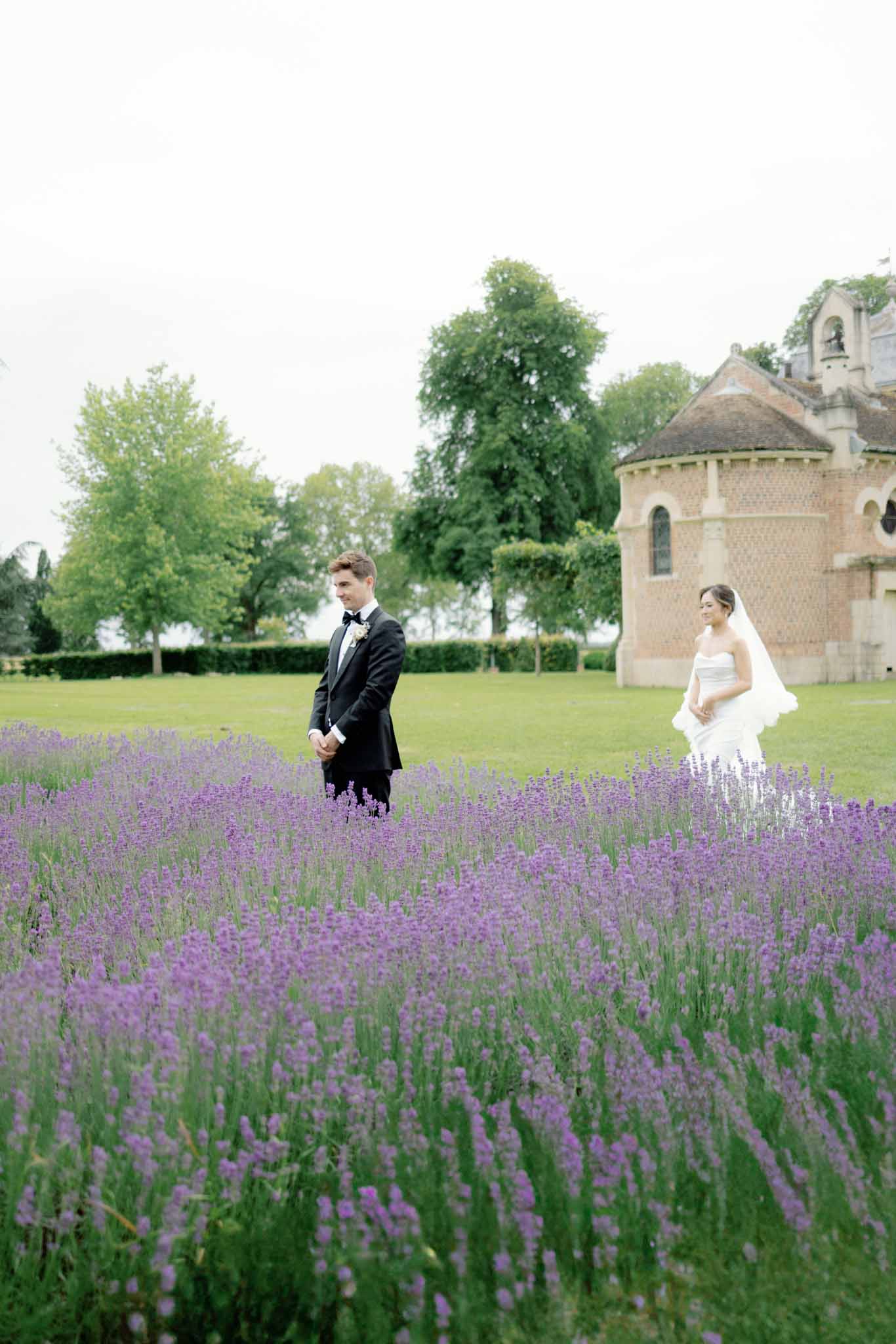 Bride and groom posing in a lavender field with a stone church and countryside landscape in the background