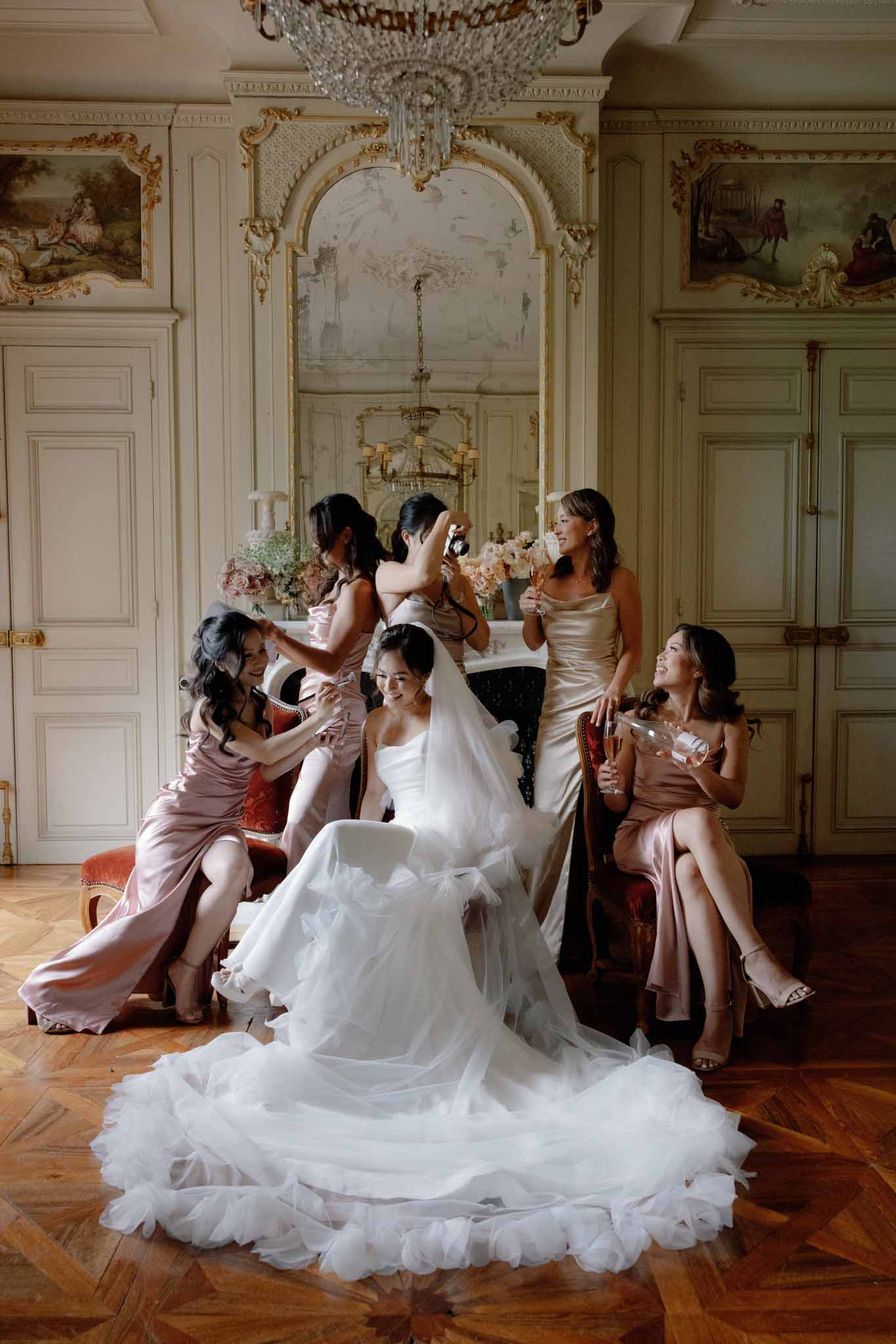 Bride in ivory tulle gown with six bridesmaids in dusty rose satin in neoclassical ballroom with crystal chandelier