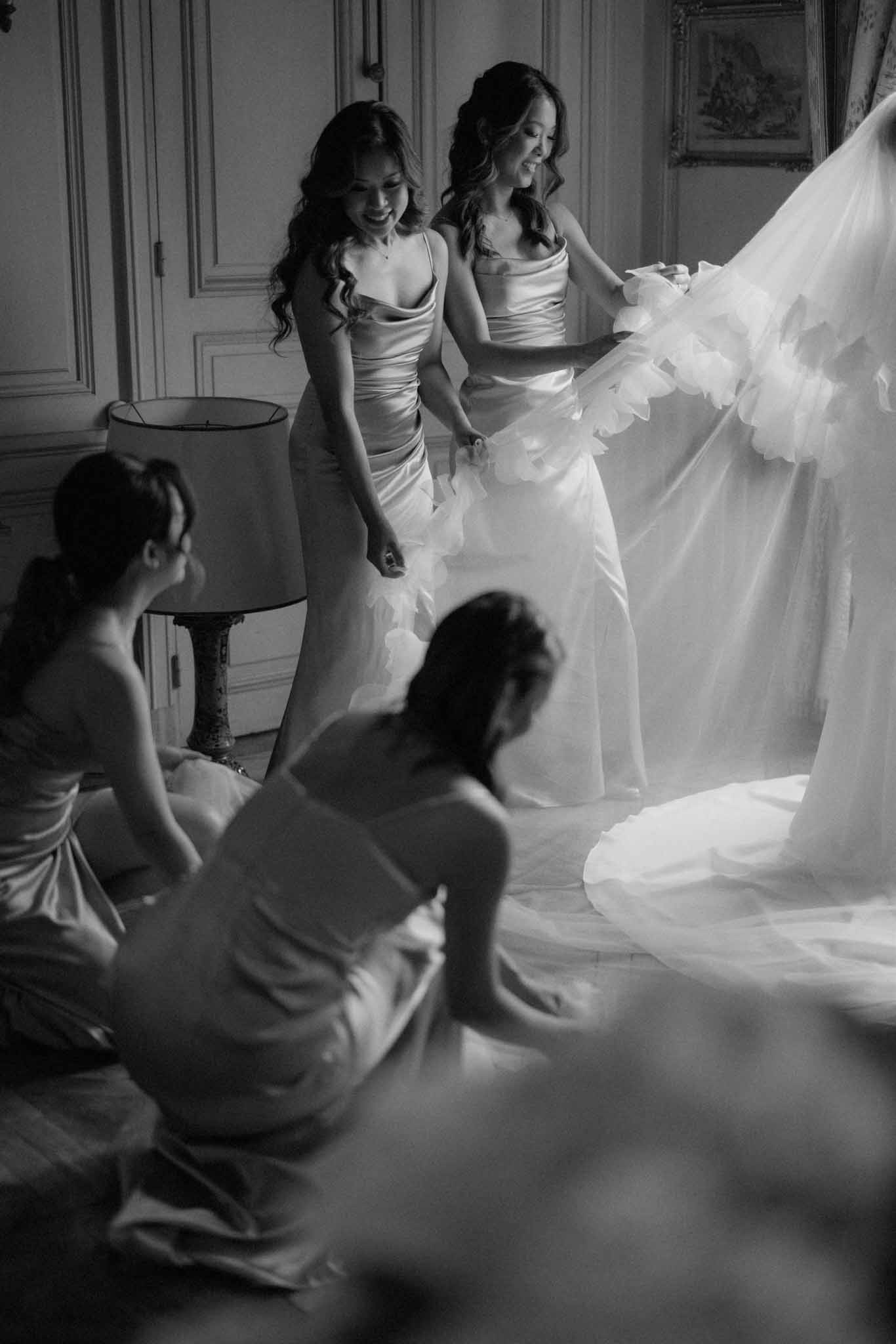 Black-and-white group portrait of bride in tulle gown with four bridesmaids in white cowl-neck dresses in formal salon