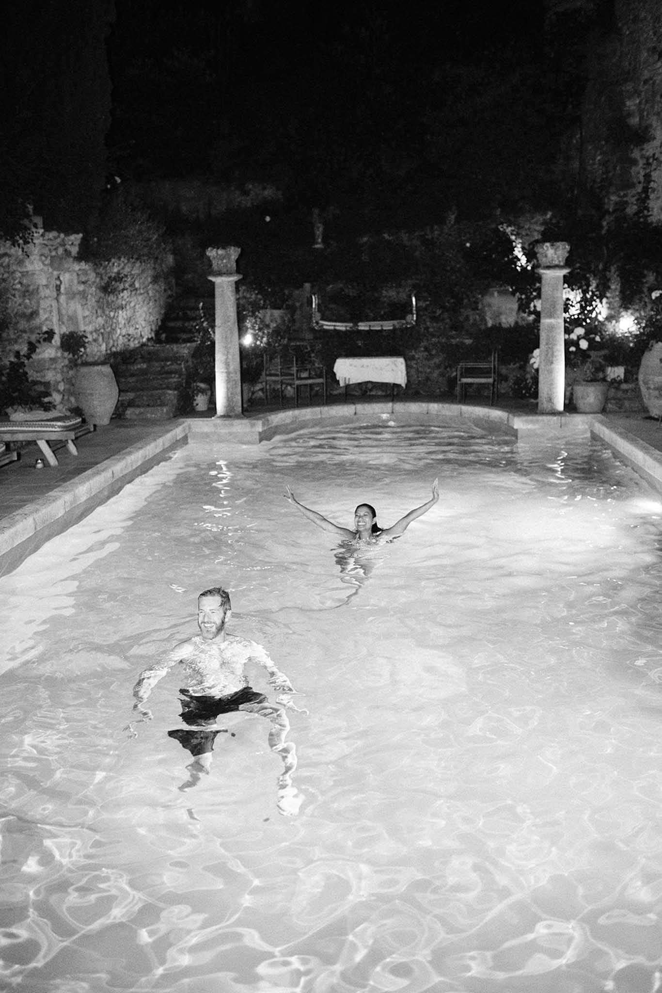 Two guests swimming in illuminated pool at night in Mediterranean courtyard, black and white photograph
