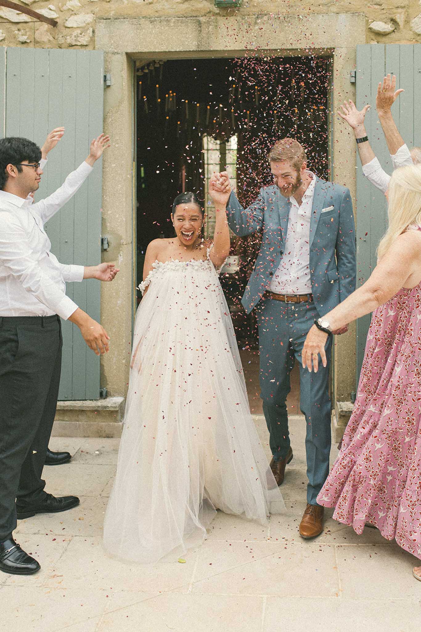 Bride and groom exiting through sage green stone doorway as guests shower them with rust and gold confetti