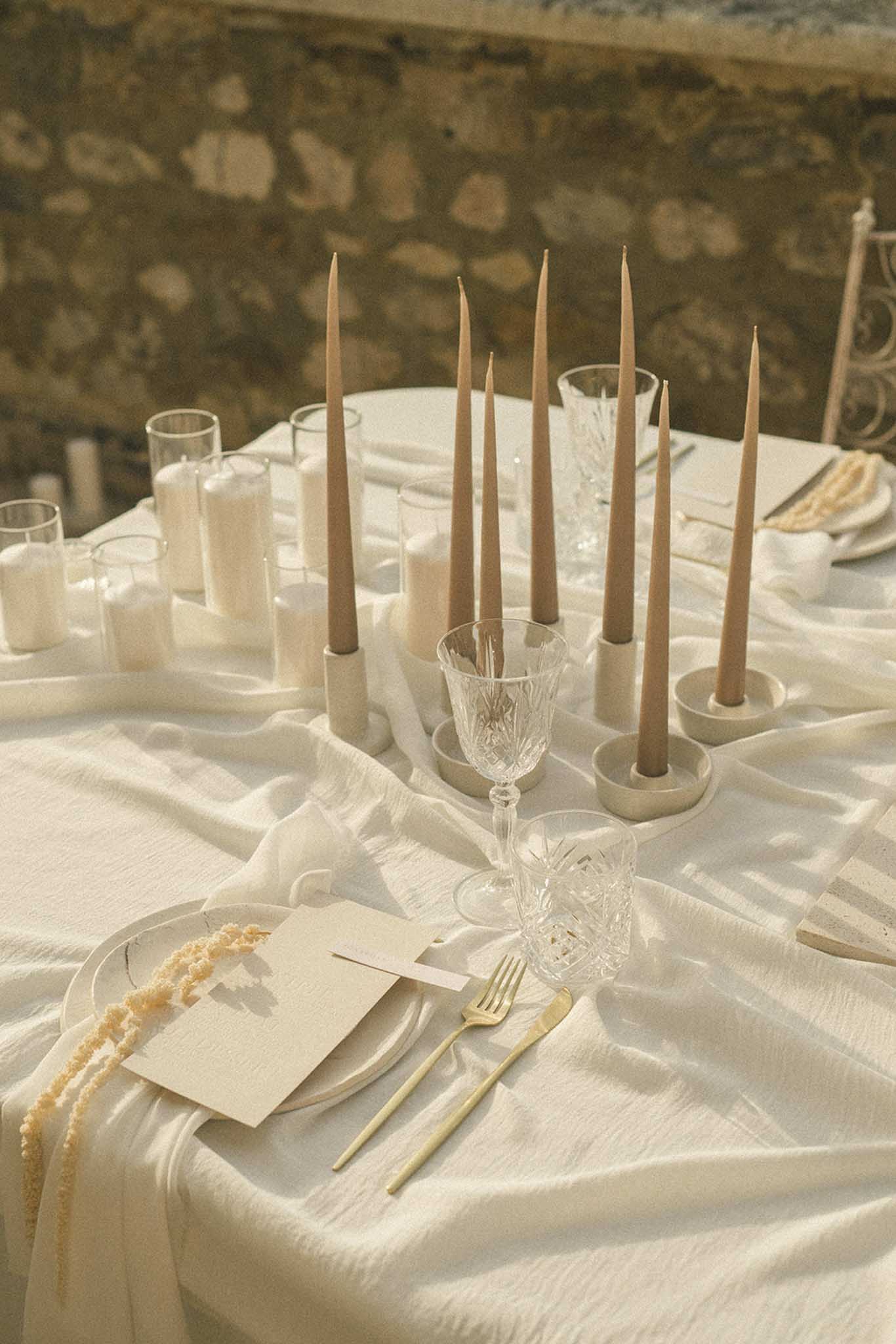 Reception table setting with gold-trimmed napkin, white taper candles in cream holders, gold flatware and cut crystal glasses