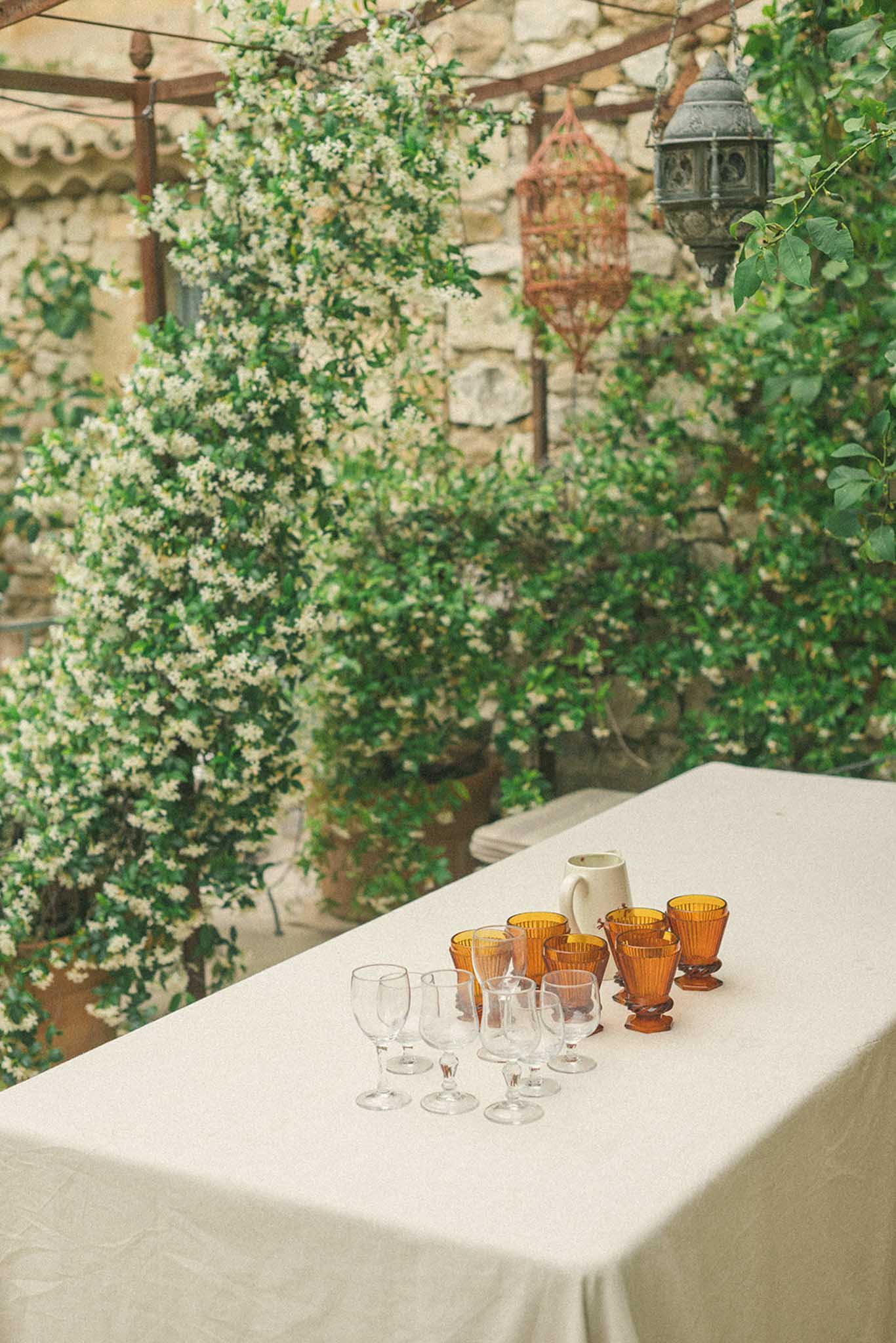 Outdoor table under pergola with cascading baby's breath, amber glassware, cream pitcher, and copper lantern above