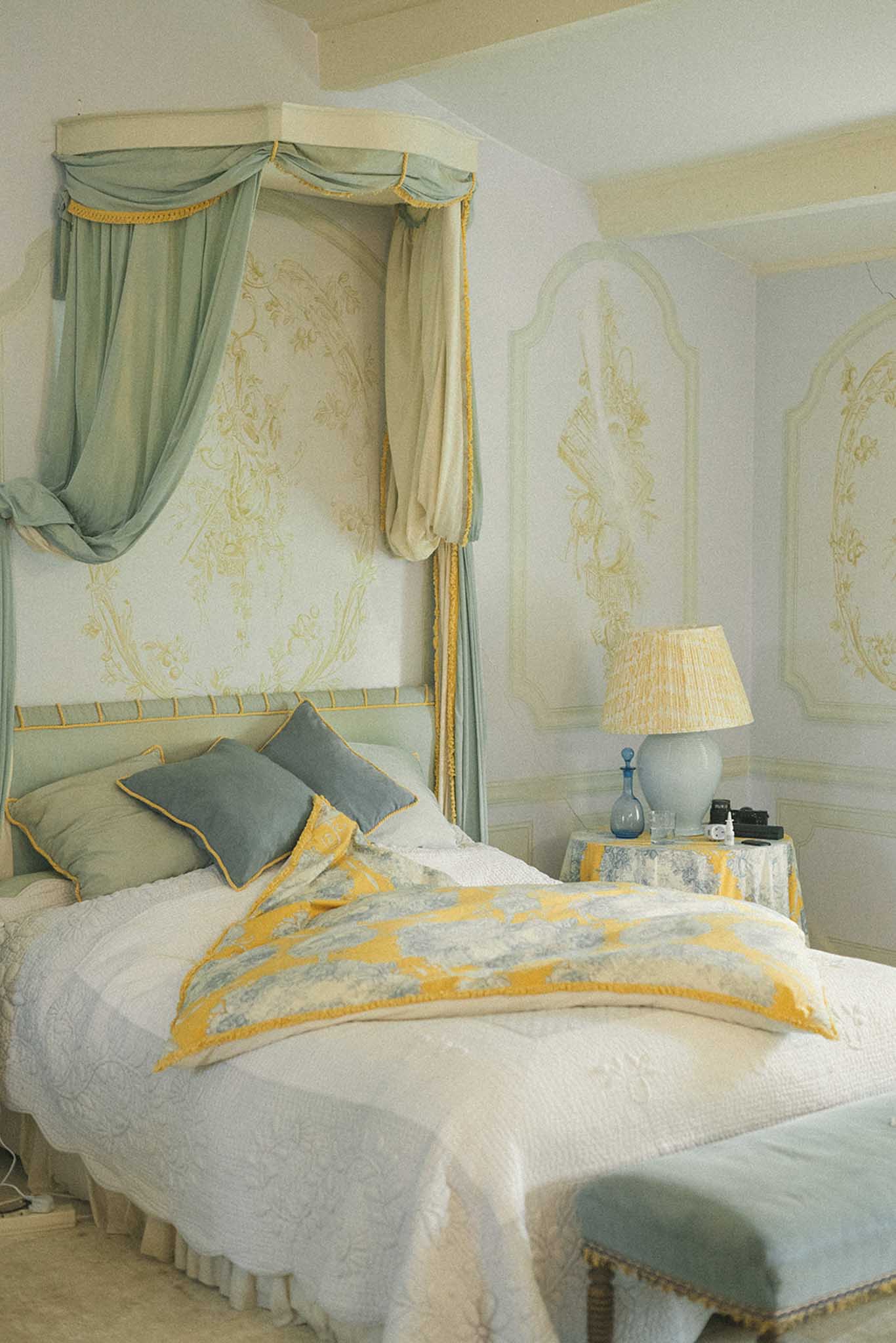 Elegantly decorated hotel bedroom with four-poster canopy bed in sage green, cream quilted bedding and toile floral wallpaper