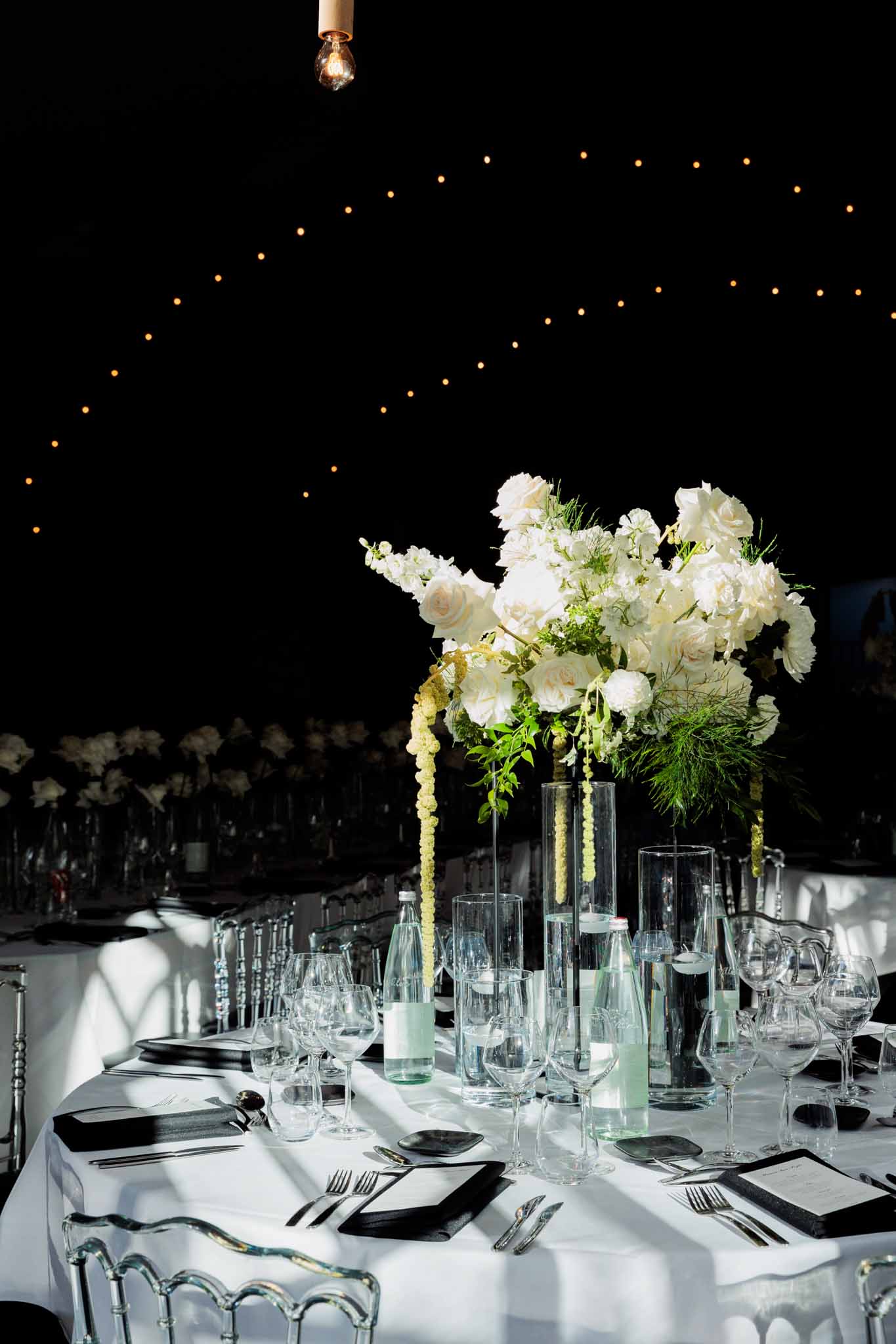 Black charger place setting with overflowing white rose and trailing amaranthus centrepiece under fairy lights