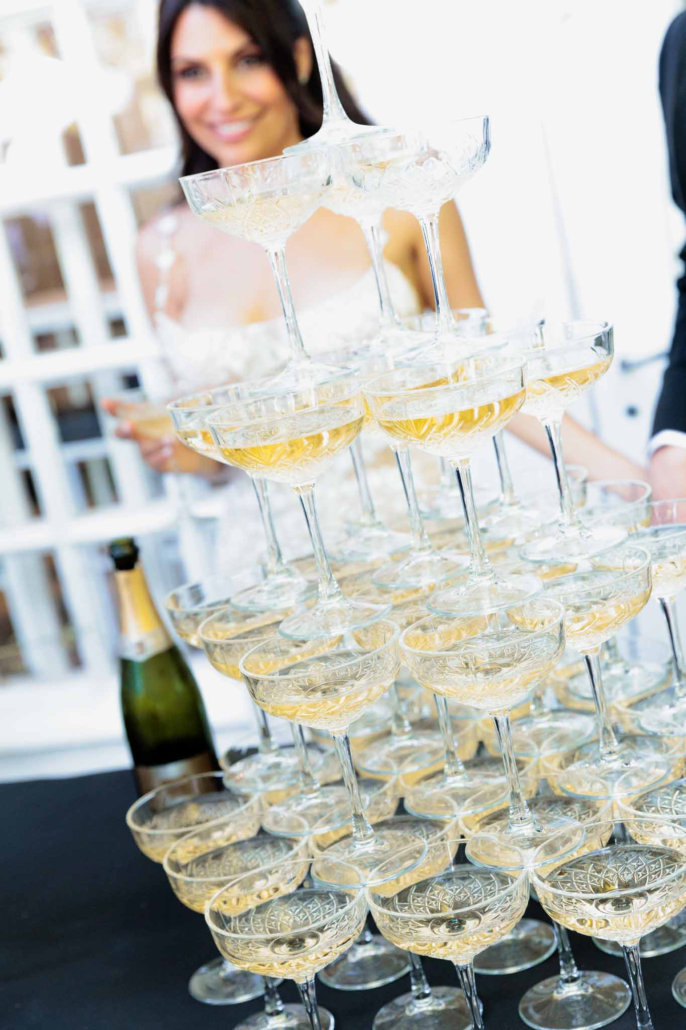 Crystal coupe champagne tower pyramid with golden champagne and bride holding glass in soft background