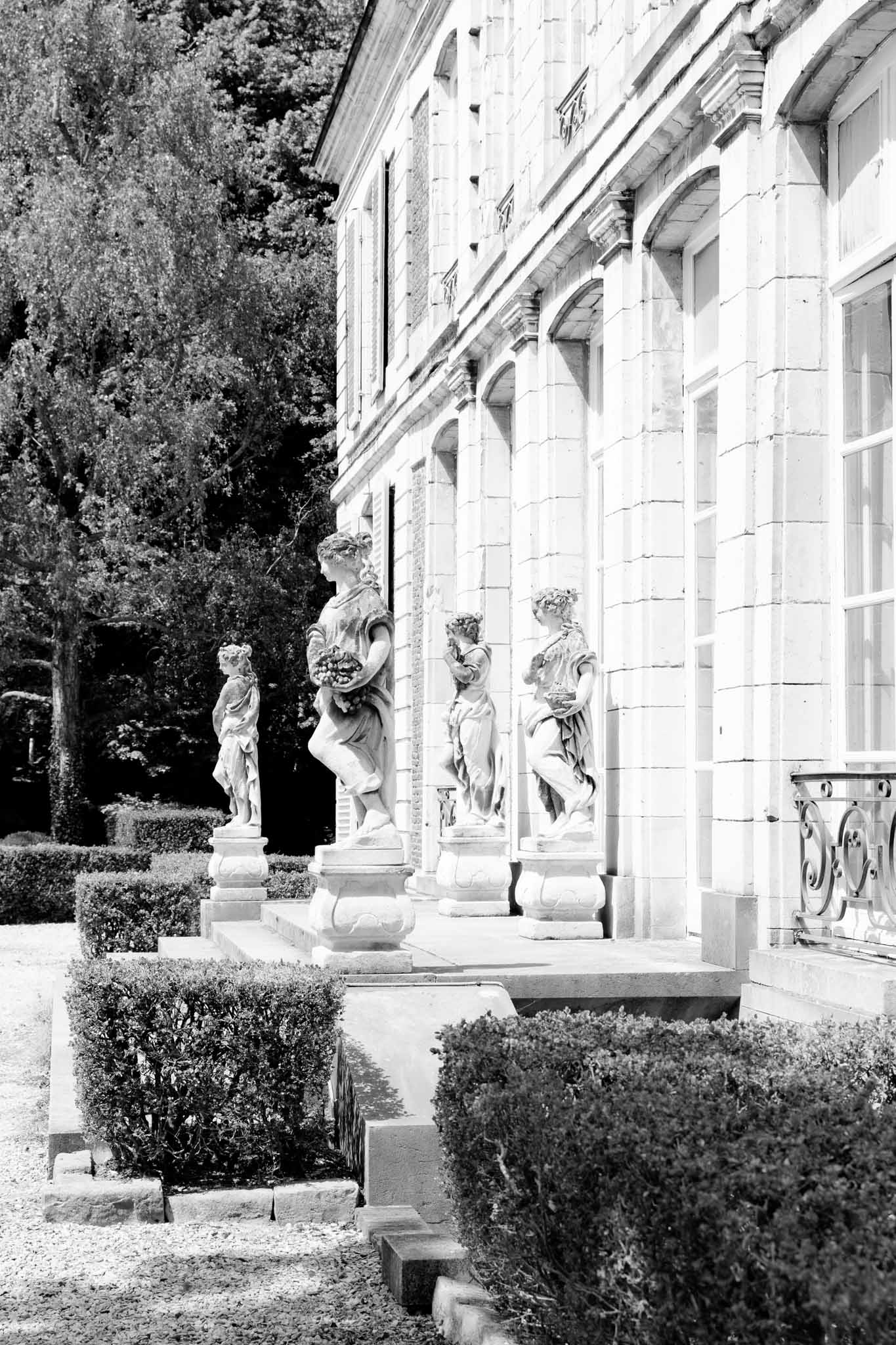Black and white view of French chateau facade with classical stone sculptures and parterre boxwood garden