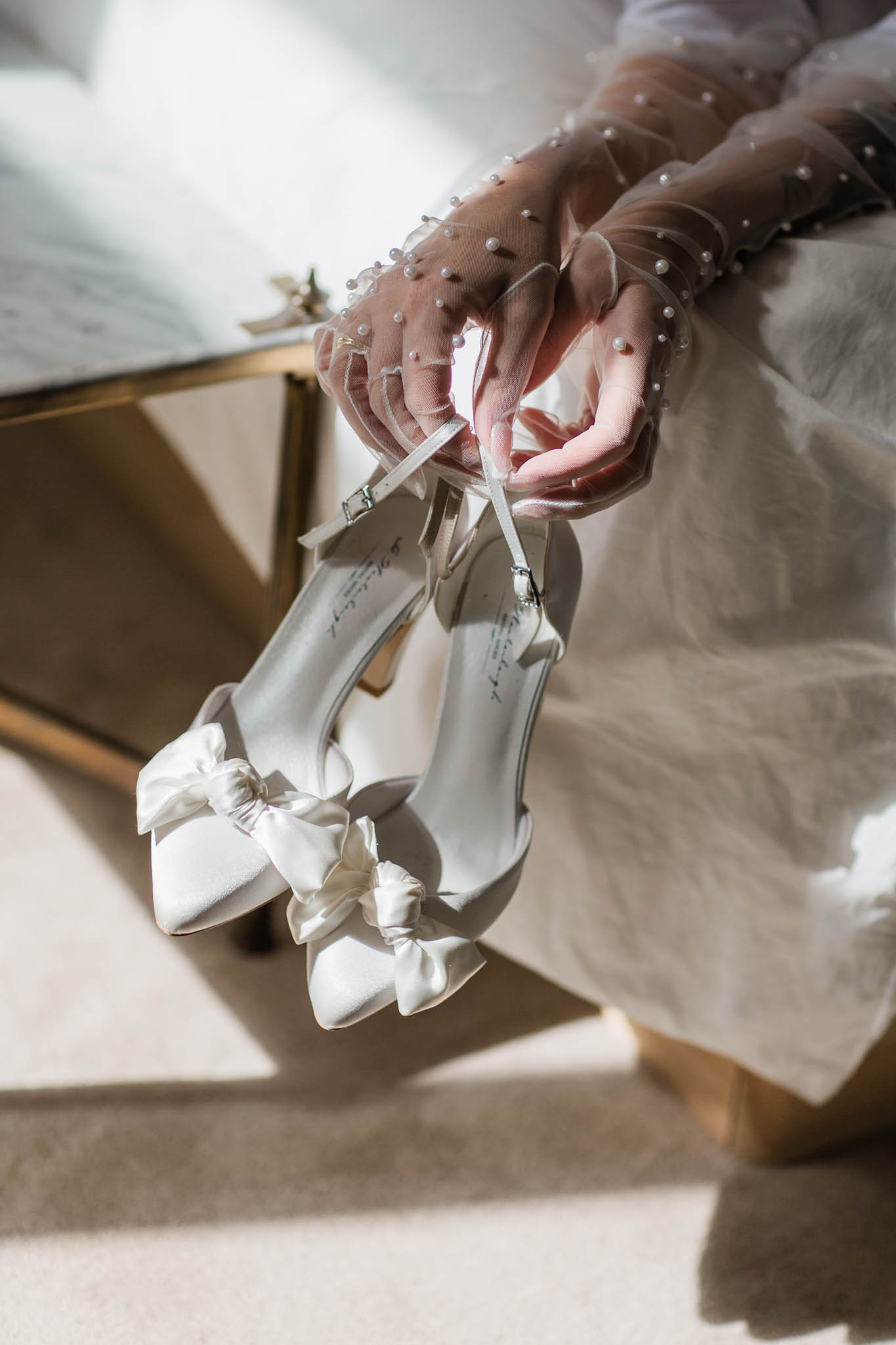 Bride's ivory heeled shoes with silk bows and mauve-pink beaded tulle gloves during wedding preparations
