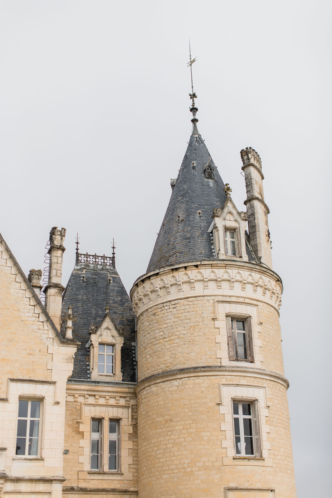 ChÃ¢teau exterior with circular tower, conical slate roof, pale golden stone, and adjacent mansard wing with decorative chimneys