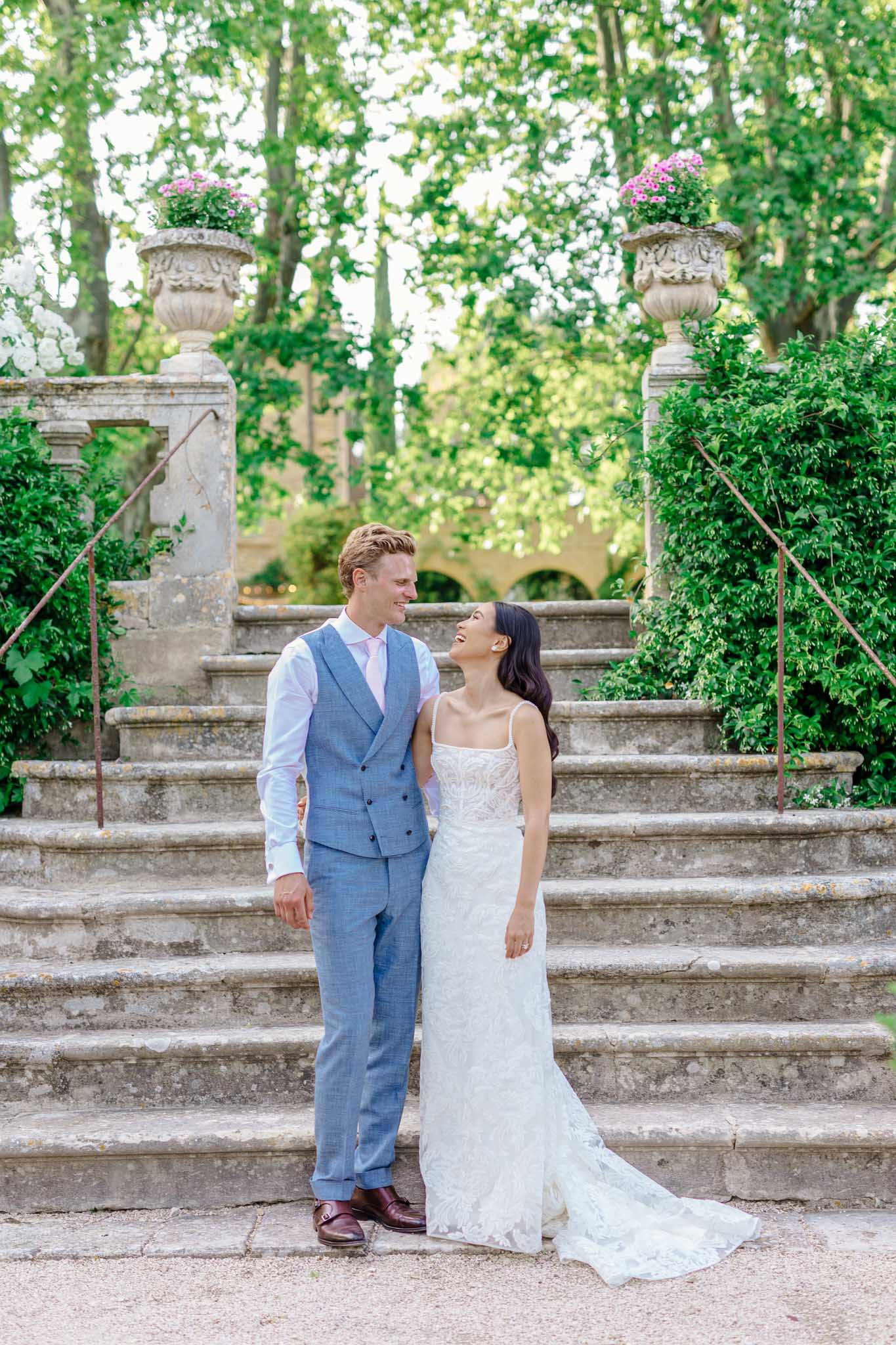 Bride and groom on formal garden staircase with groom in blue waistcoat