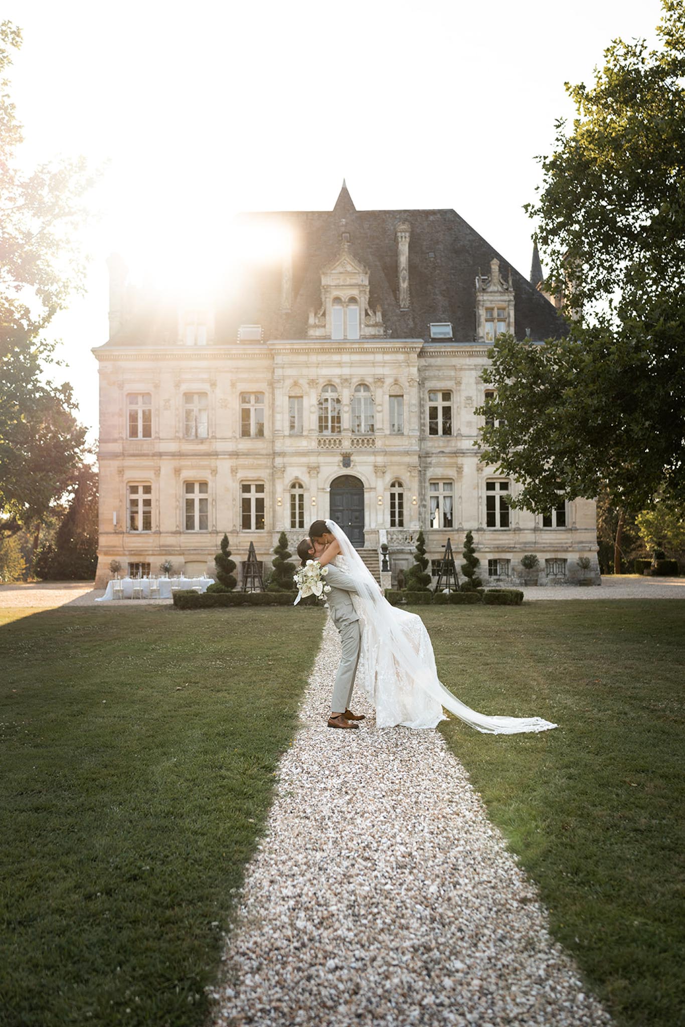 Bride and groom on gravel path at golden hour with classical French chateau behind them