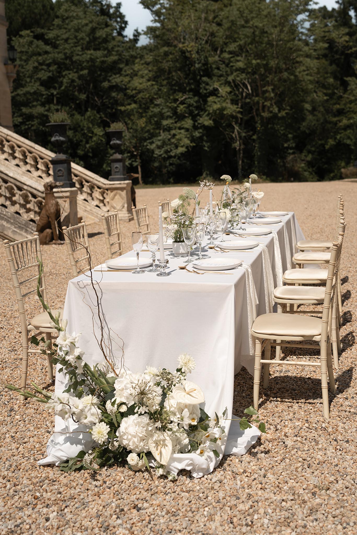 Outdoor reception table set for dinner with white dahlias, roses, and eucalyptus centerpieces in courtyard