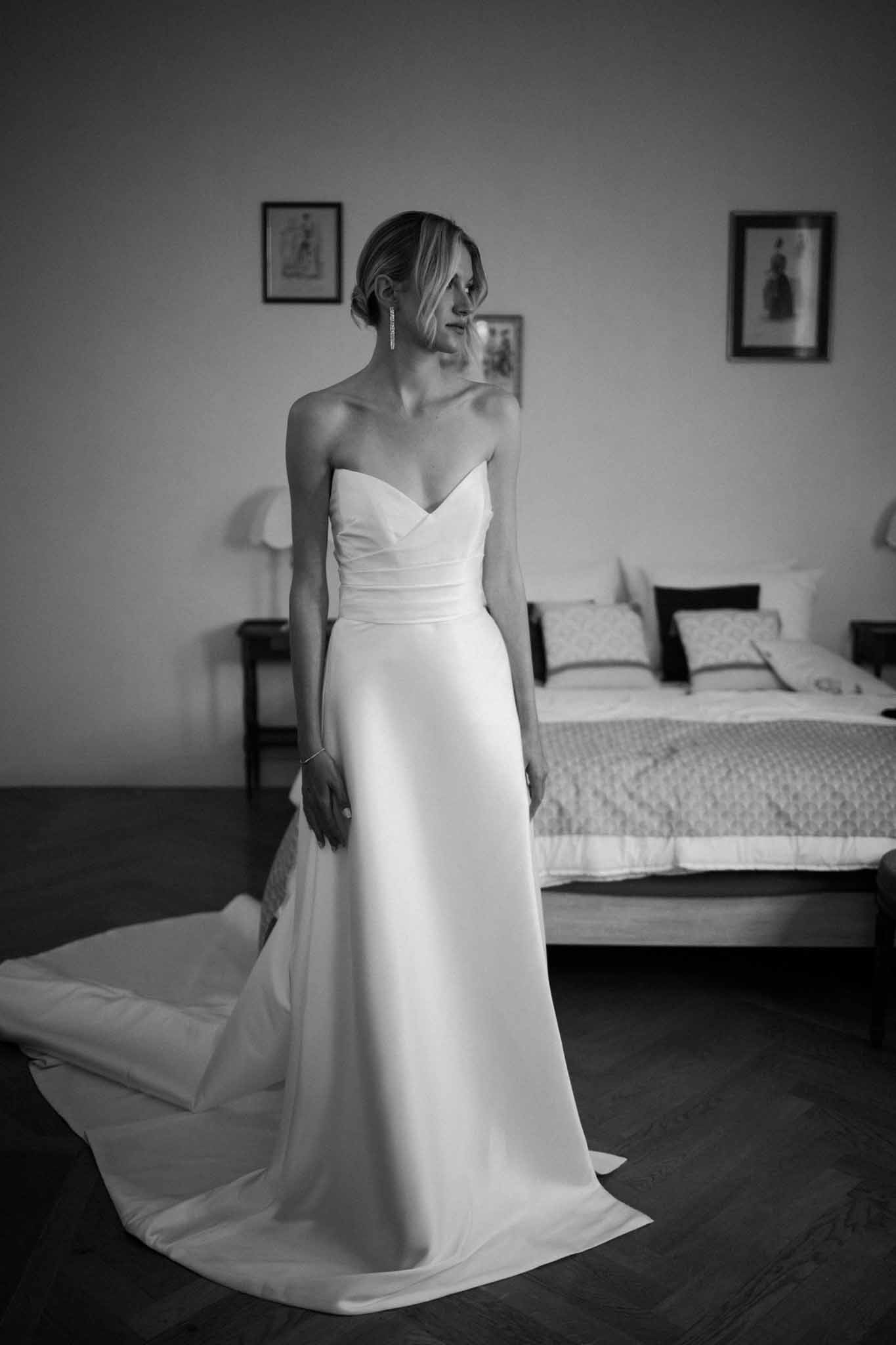 Black-and-white portrait of bride in strapless ruched gown in bedroom during getting ready