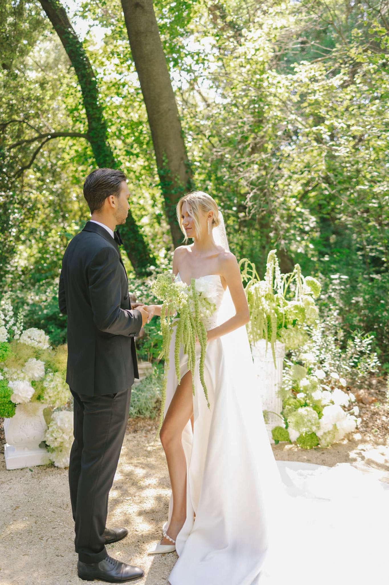 Couple exchanging vows in wooded garden with white hydrangea and green amaranthus in ceramic urns
