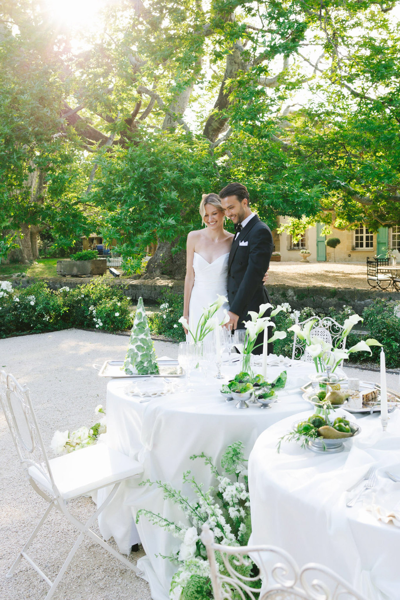 Bride and groom at outdoor reception with round tables, white gardenias, and yellow manor house