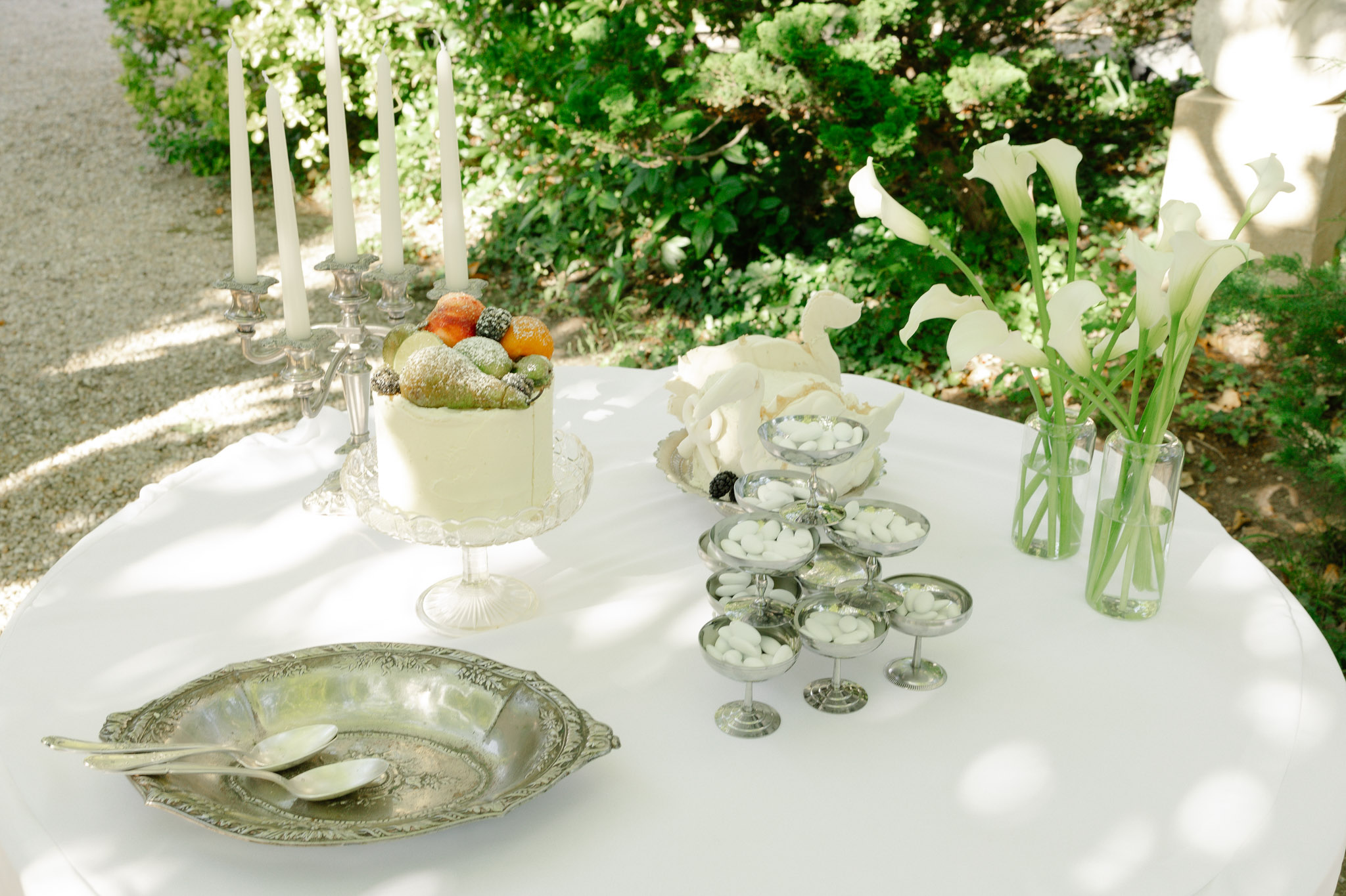 Outdoor reception table with calla lily centerpiece, silver candelabra, tiered pale yellow cake and linen-covered table