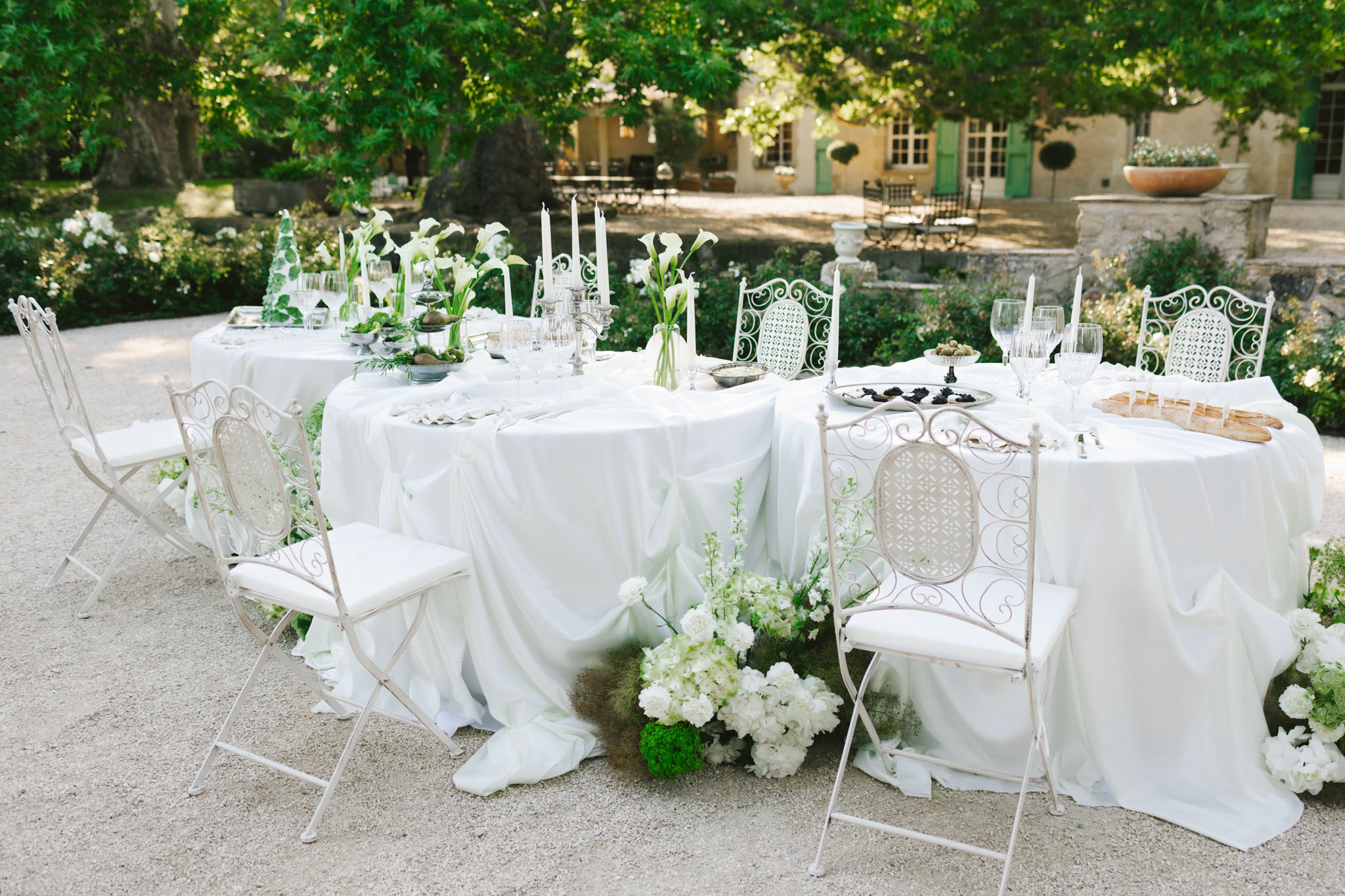 Outdoor round reception tables with white linens, silver candelabras, white hydrangeas, and ornate wrought-iron chairs