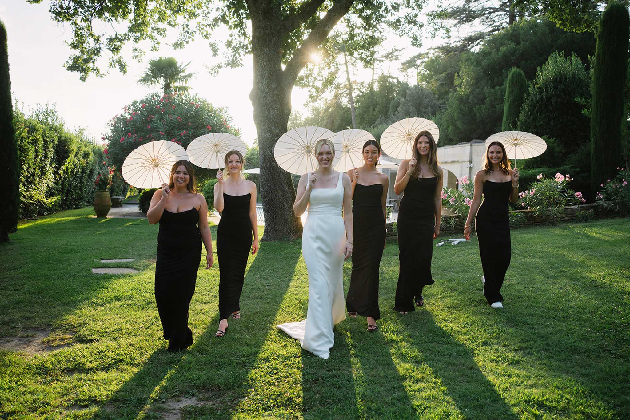 Bride with bridesmaid in black dress holding white umbrella outdoors at ChÃ¢teau de Fontareches