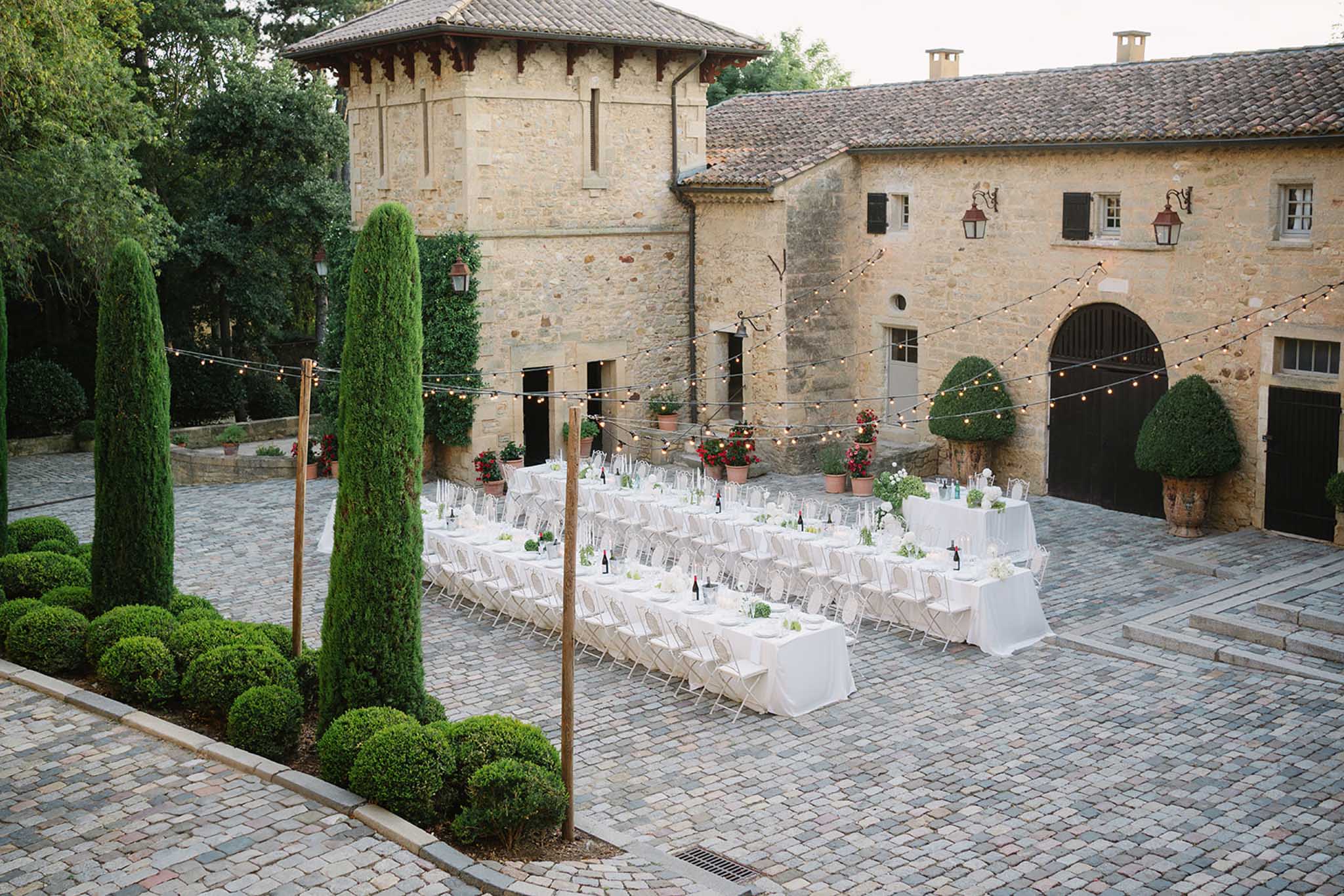 Wedding reception tables with string lights in historic stone courtyard with central tower