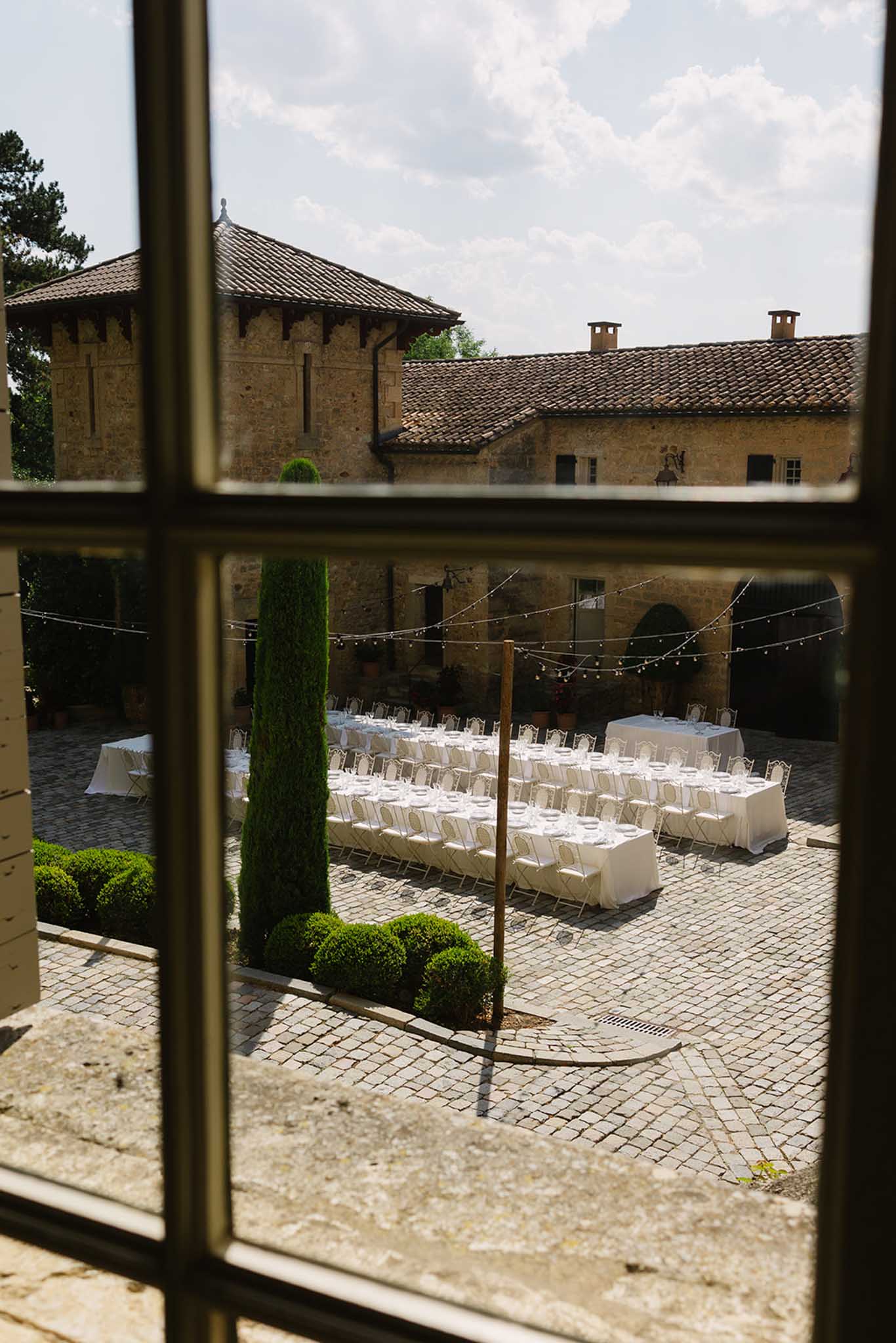 Reception setup at ChÃ¢teau de Fontareches viewed through glass window showing tables and floral decor
