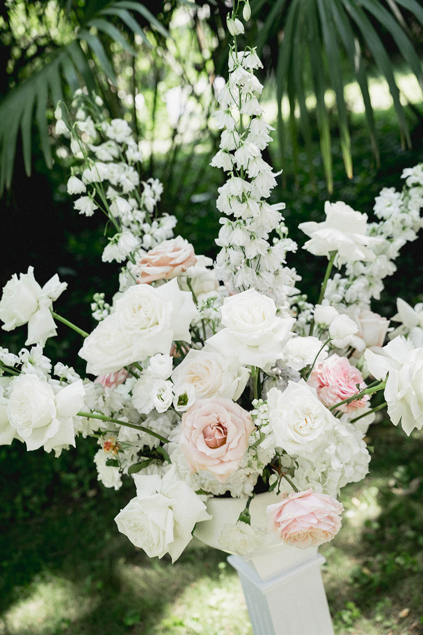 Close-up of garden wedding floral arrangement with ivory and blush roses, white delphinium, and baby's breath