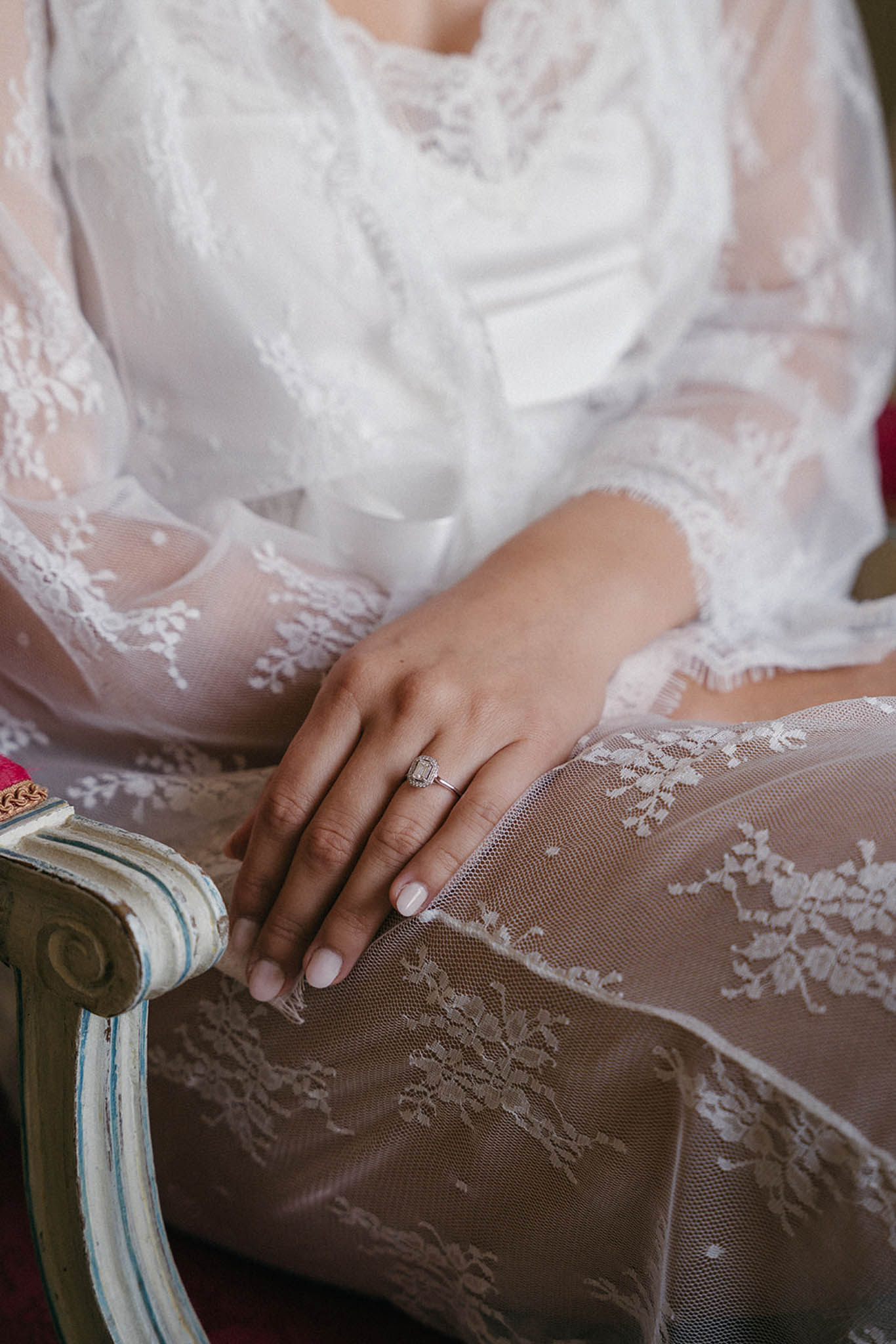 Close-up of bride's hand showing diamond engagement ring and wedding band, wearing ivory lace long-sleeve gown