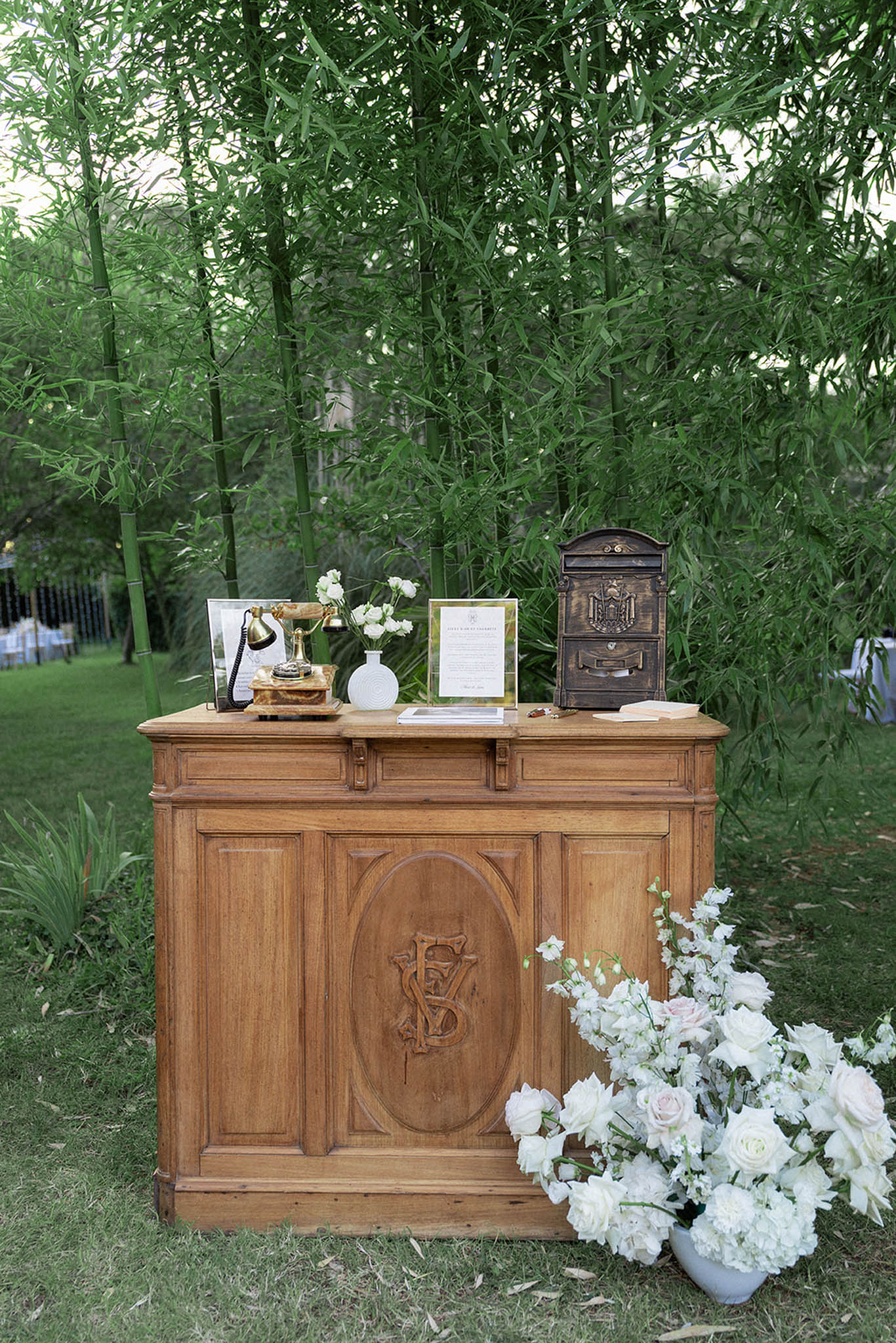 Welcome table with antique rotary telephone, white roses in ceramic urn, and vintage accessories in garden