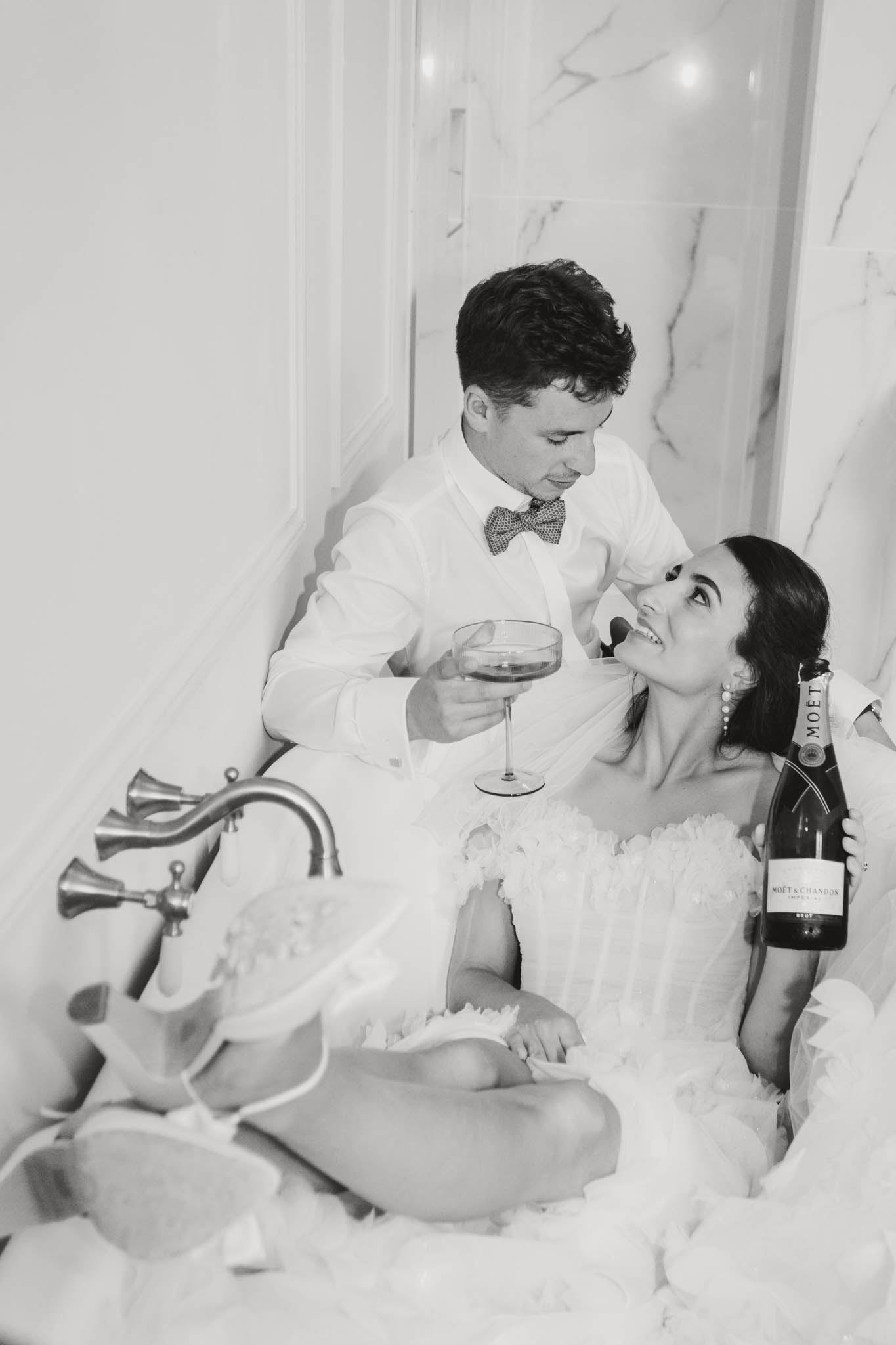 Bride and groom sitting together in bathtub holding wine glasses, black and white photo at ChÃ¢teau de Londigny