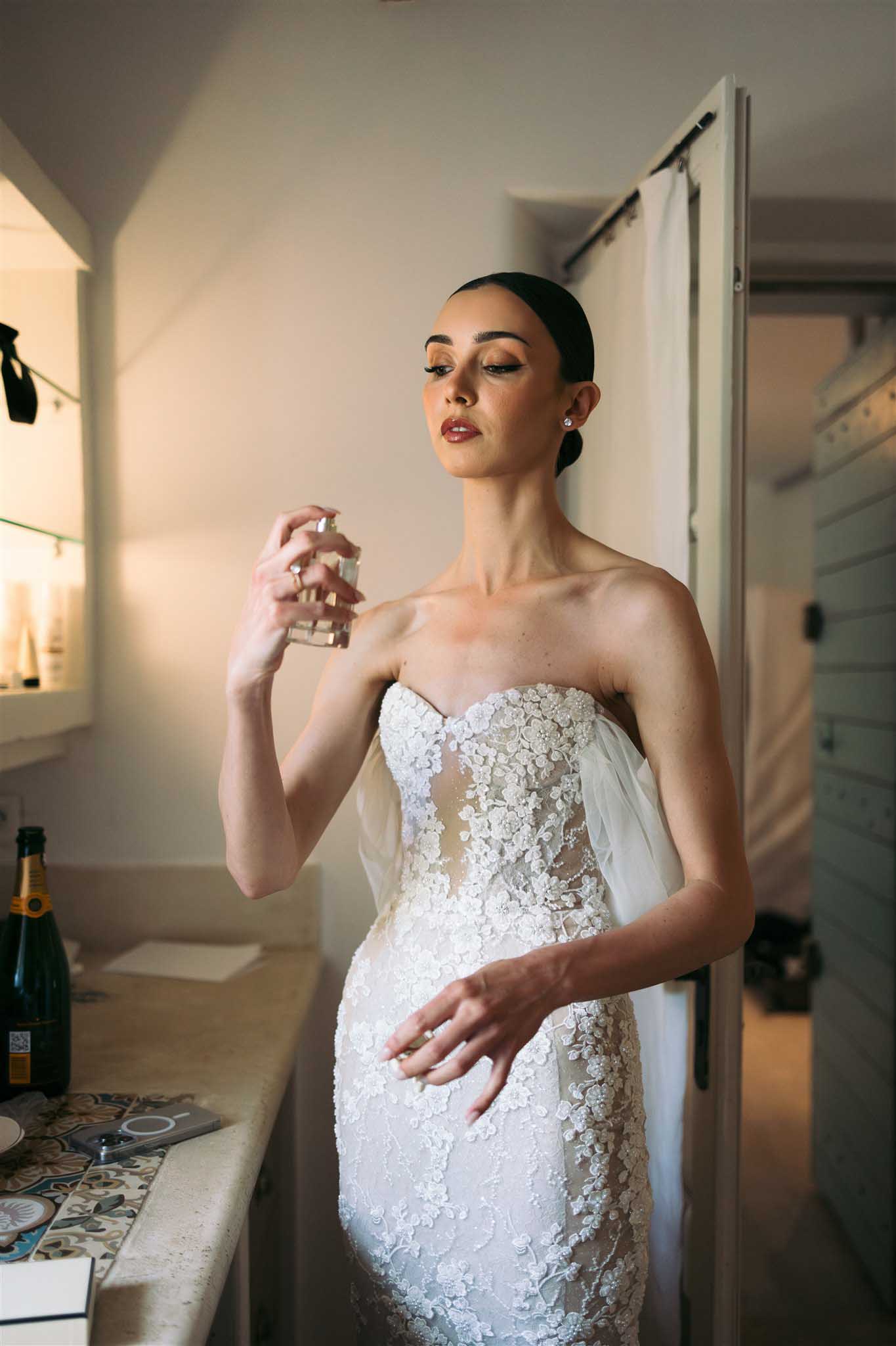 Bride applying perfume in strapless beaded gown with floral appliques during getting ready