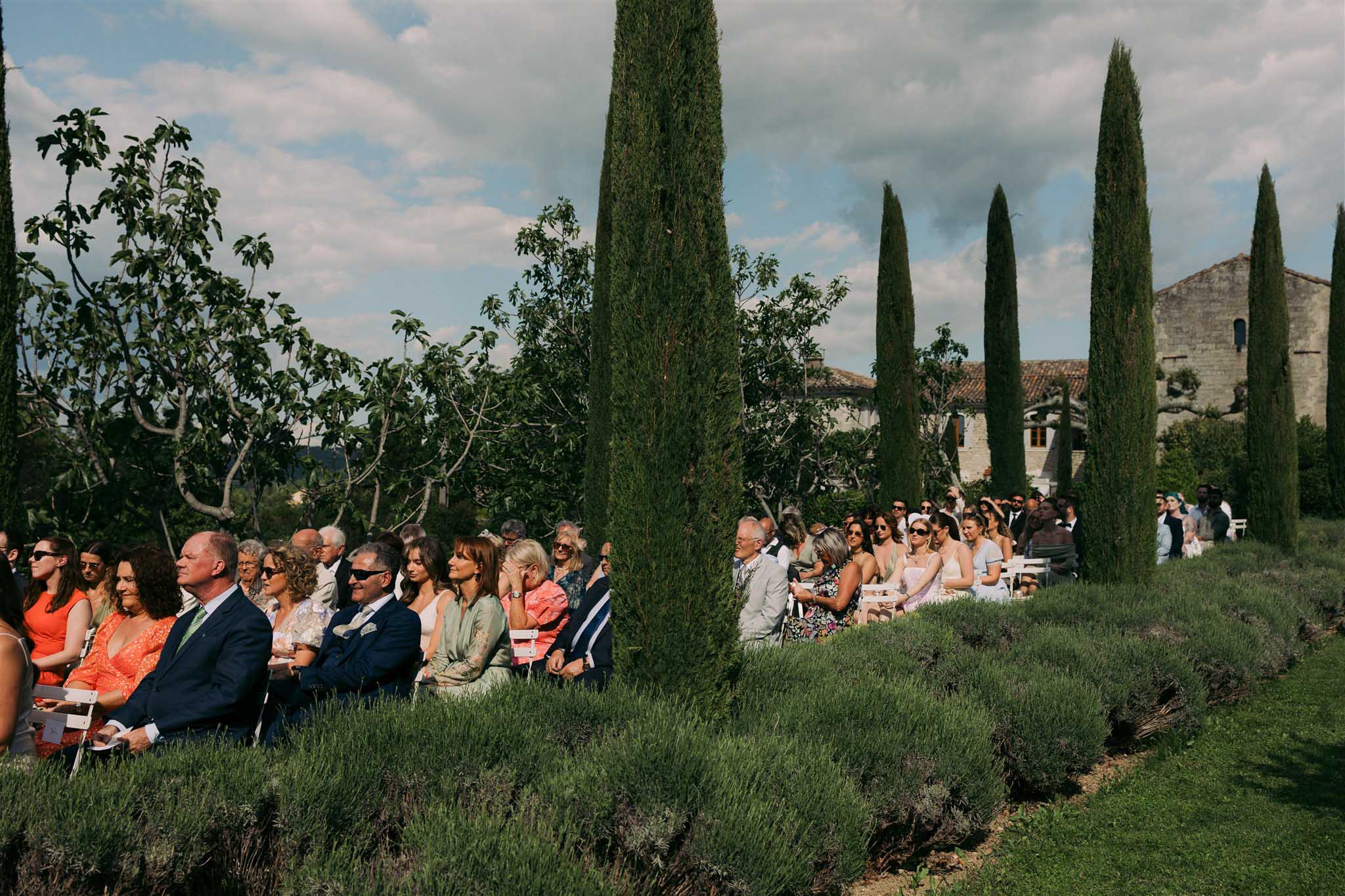Guests seated for outdoor ceremony at Abbaye Saint-EusÃ¨be surrounded by pine trees and wild plants