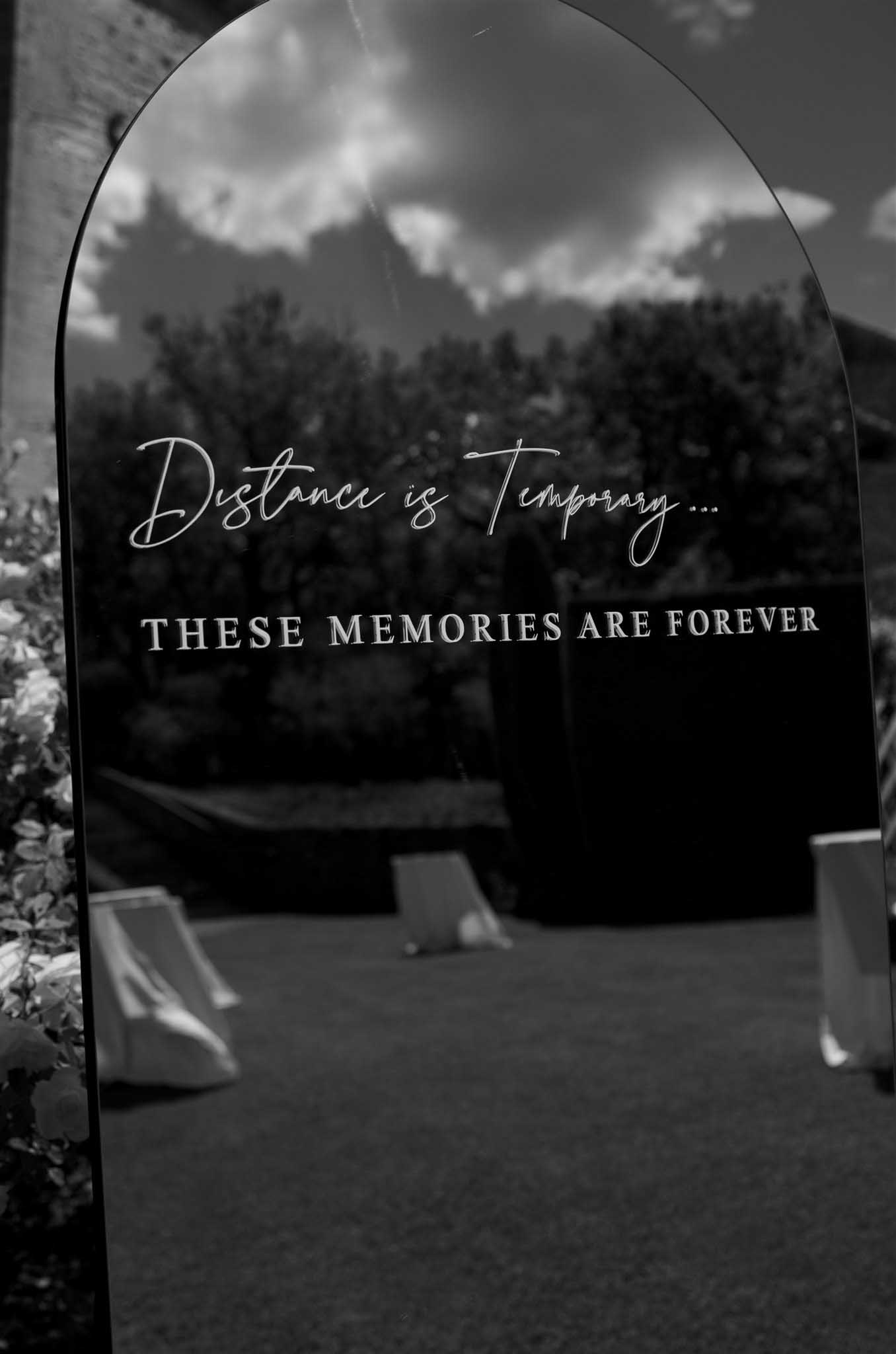 Decorative wedding arch with engraved sentiment text against mountainous forested landscape, black and white photo