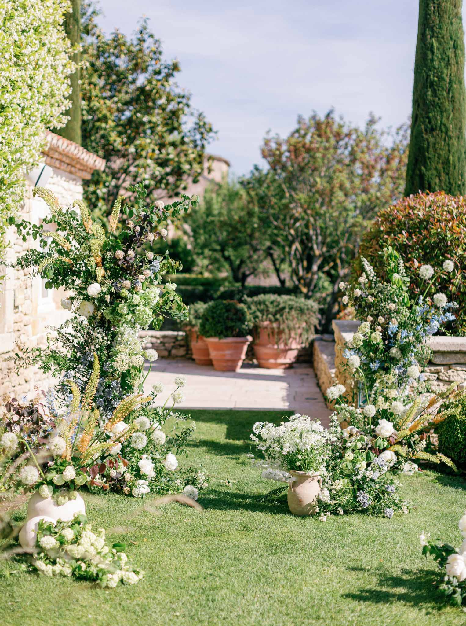 Formal garden ceremony setup with white flowering urns and cypress trees at a stone Provencal estate