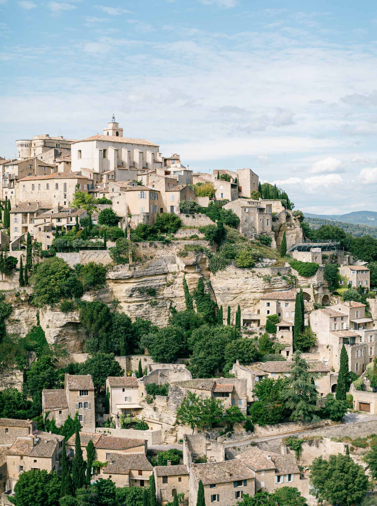 Aerial view of a hilltop Provencal village with stone buildings and church bell tower against distant mountains