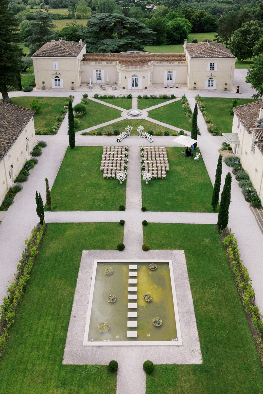 Aerial view of a ceremony setup with white chairs and floral arch in formal French chateau gardens