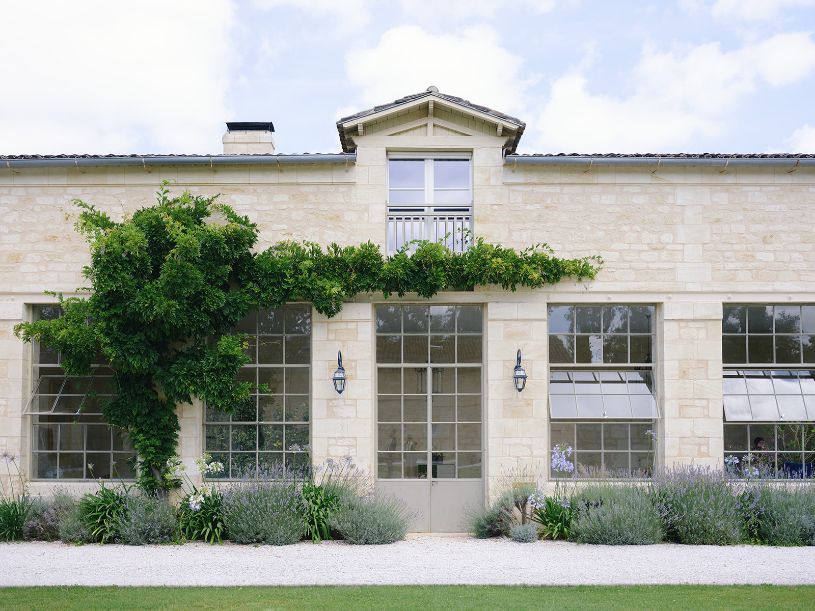 French country stone building with symmetrical tall windows, climbing ivy, and lavender beds along facade