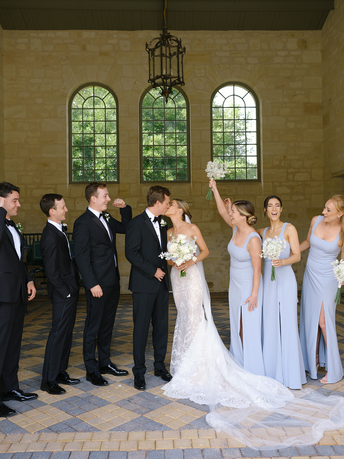 Bridal party portrait with bridesmaids in periwinkle dresses and groomsmen in black tuxedos in arched venue