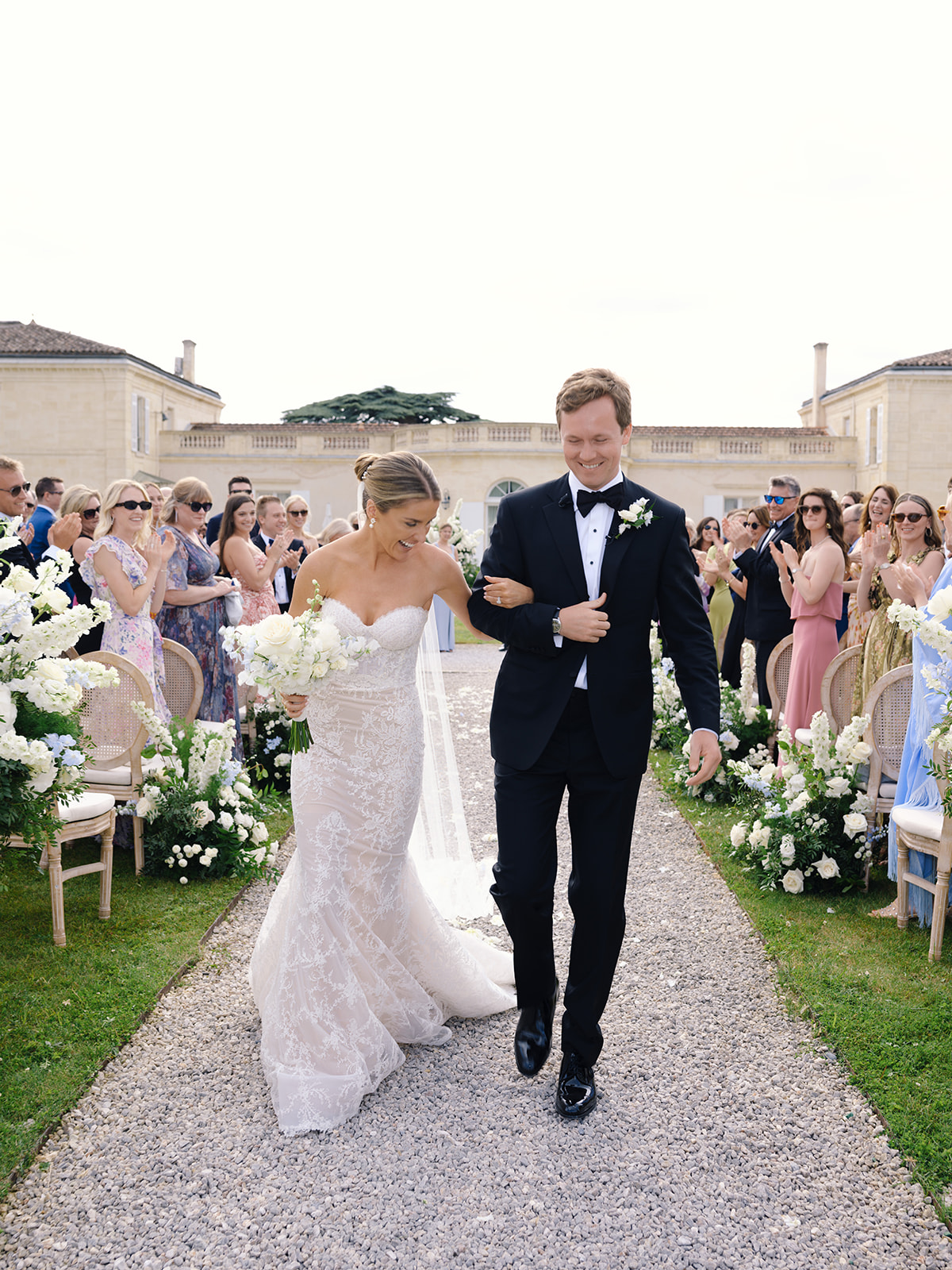 Bride and groom walking down outdoor aisle after ceremony with guests applauding at stone manor