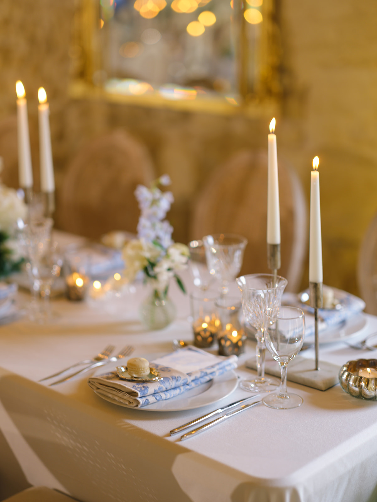 Formal table setting with blue striped napkins, gold candlesticks, white flowers and crystal glassware on white linen