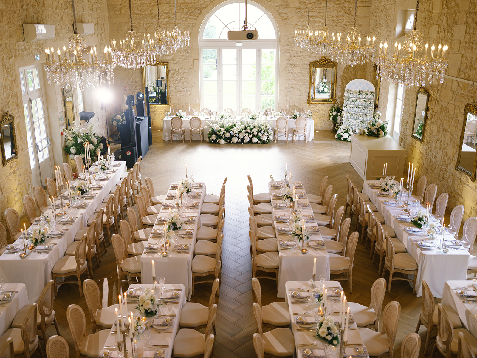 Indoor ballroom reception with crystal chandeliers, ivory linens, and white floral centerpieces