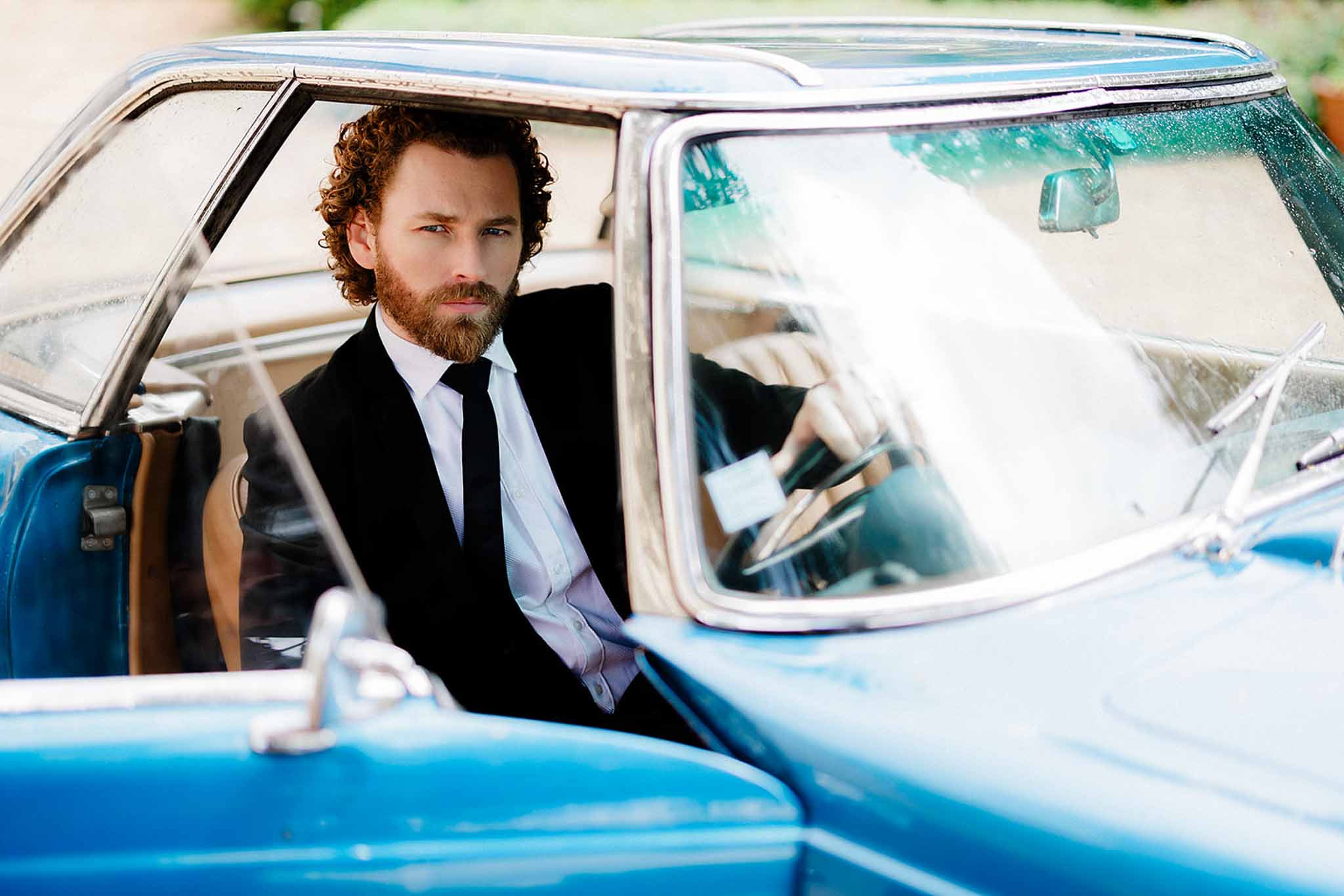 Groom sitting inside vintage blue and white convertible car