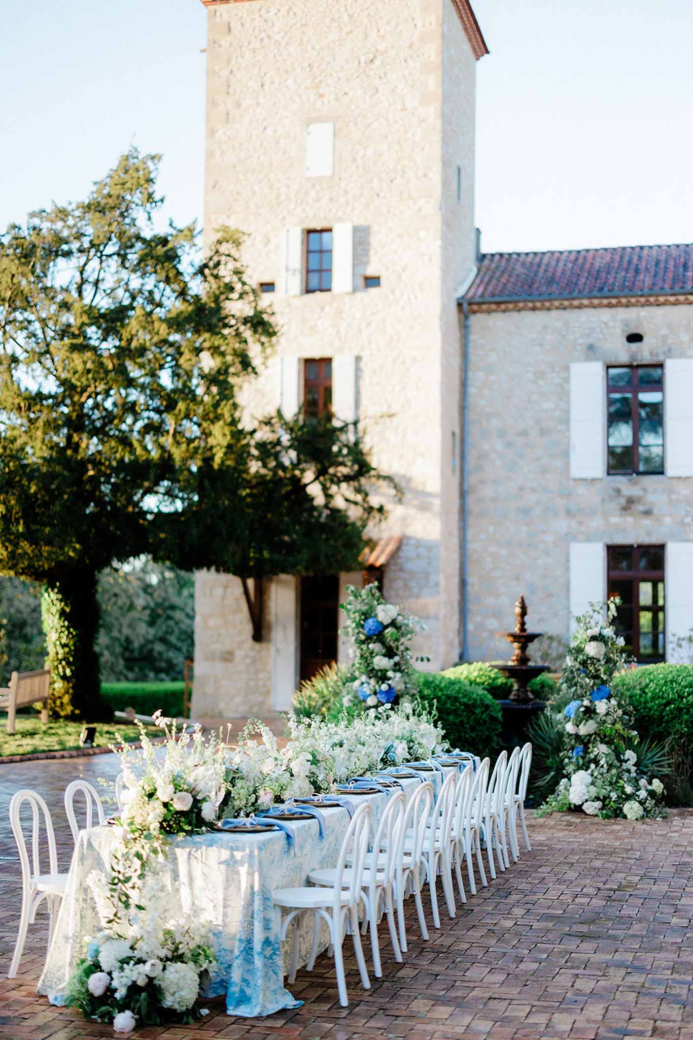 Long reception table set outside manor at ChÃ¢teau de Trieux with guests and bride and groom