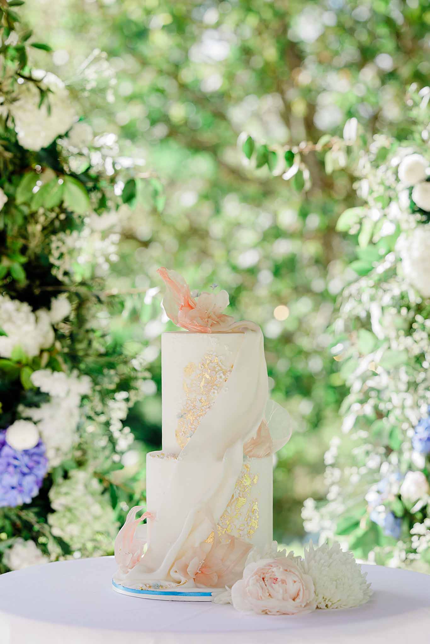 Three-tiered ivory wedding cake with gold leaf accents and peach sugar flower topper