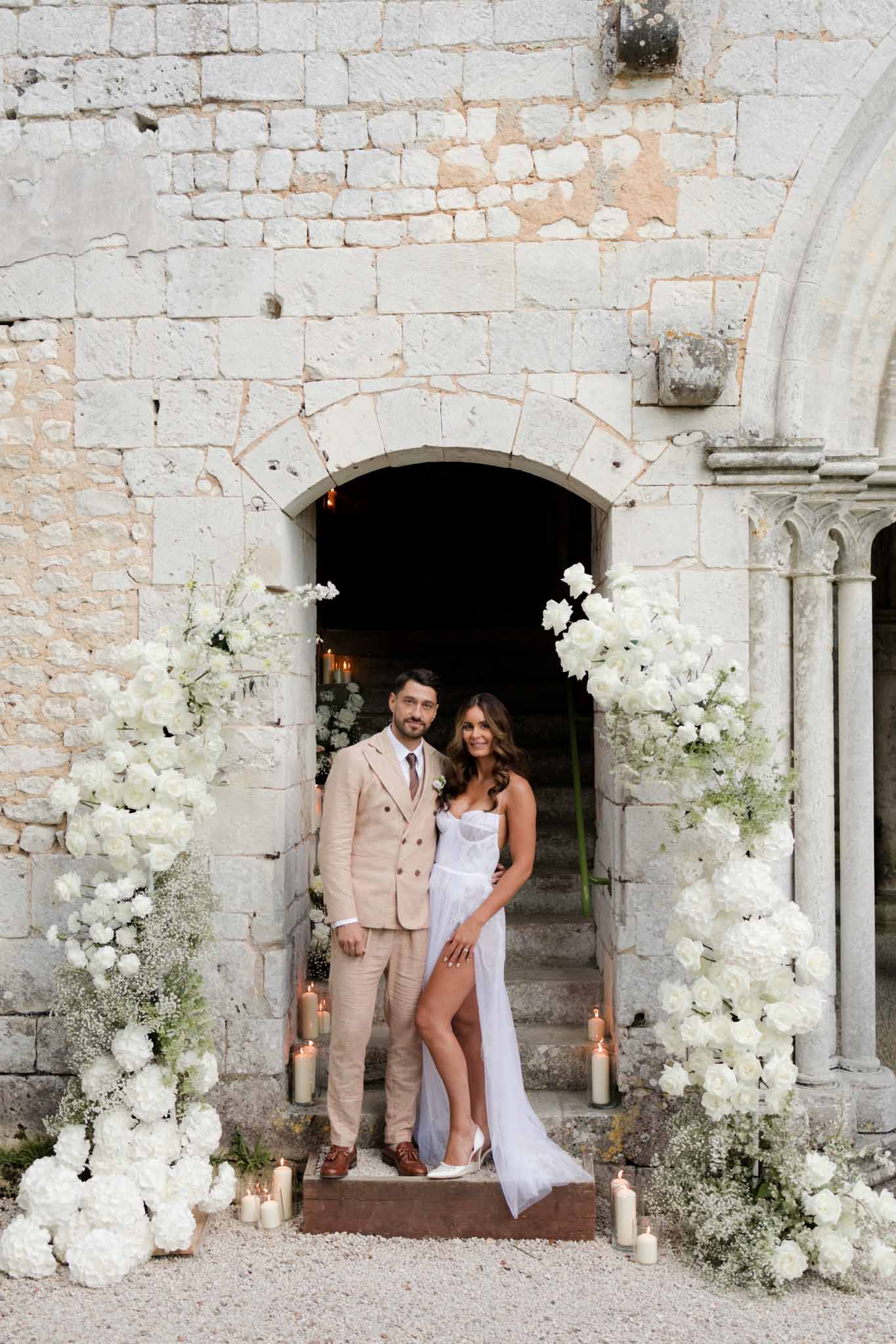 Bride and groom at stone chapel entrance flanked by white peony and eucalyptus installations