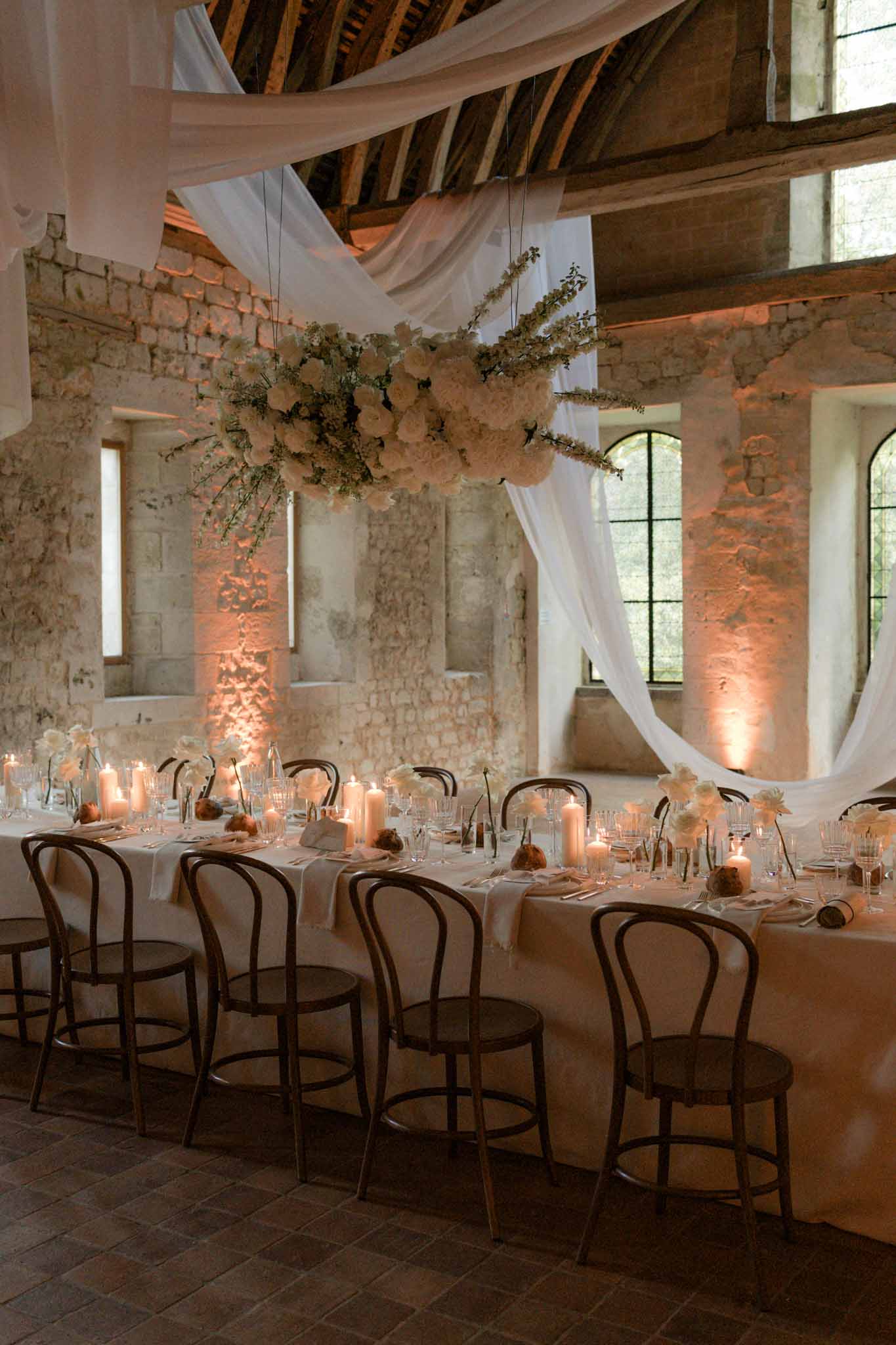 Reception banquet table in stone barn with suspended floral installation in blush and cream with draped fabric panels