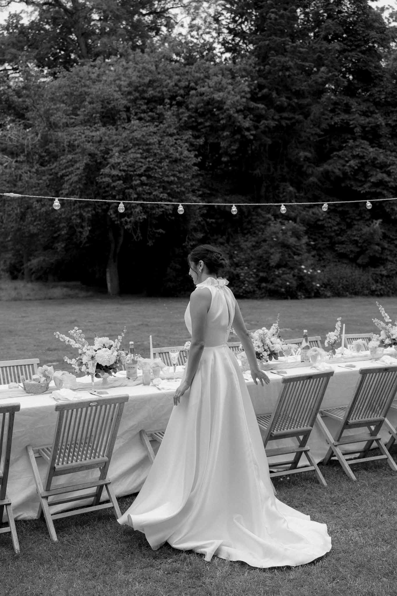 Black-and-white bride viewed from behind surveying outdoor reception dining setup