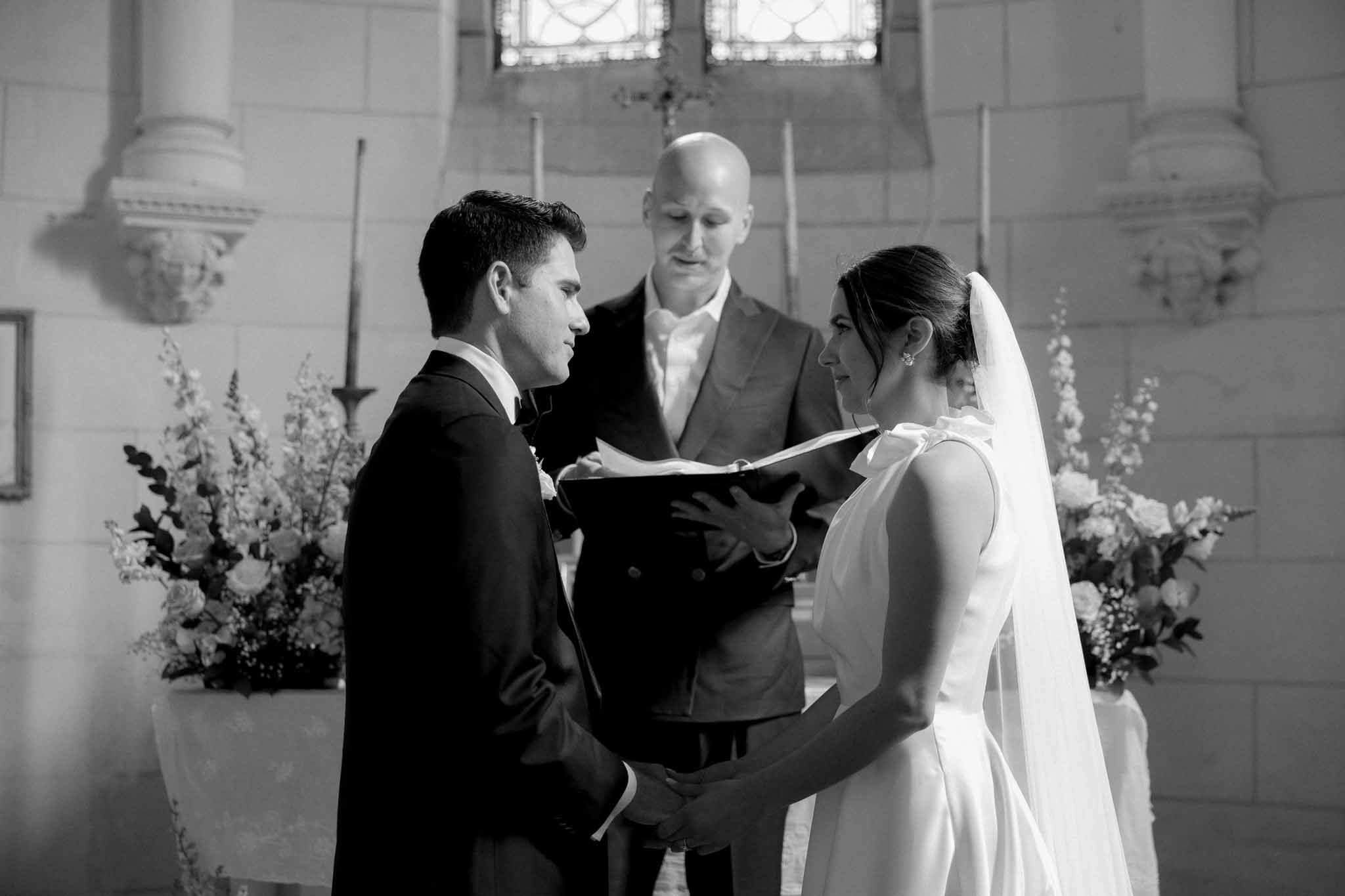 Black-and-white ceremony in classical chapel with officiant reading to couple at altar