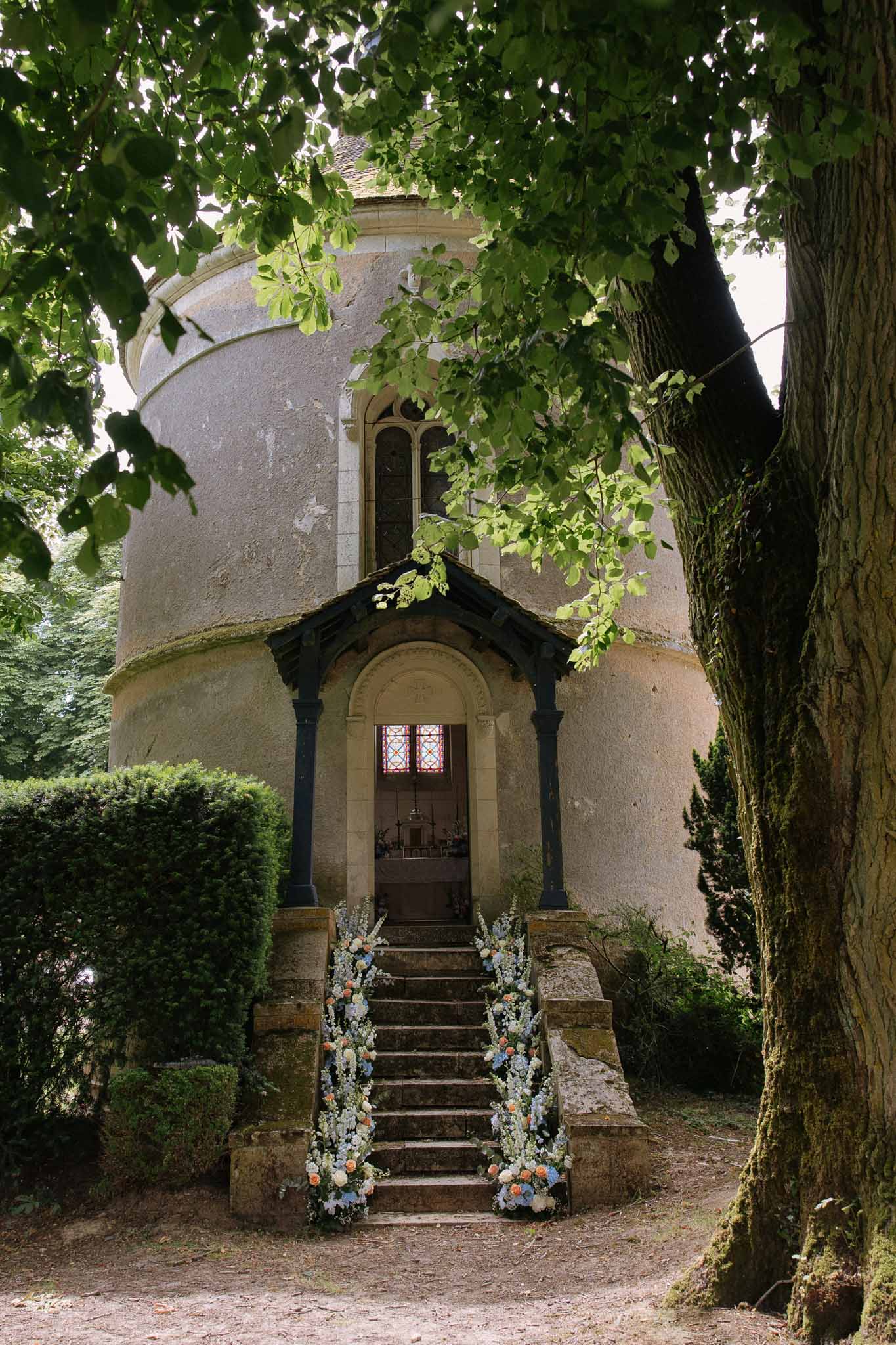 Historic stone chapel entrance with rounded tower, floral garlands on stairway and stained glass arch doorway