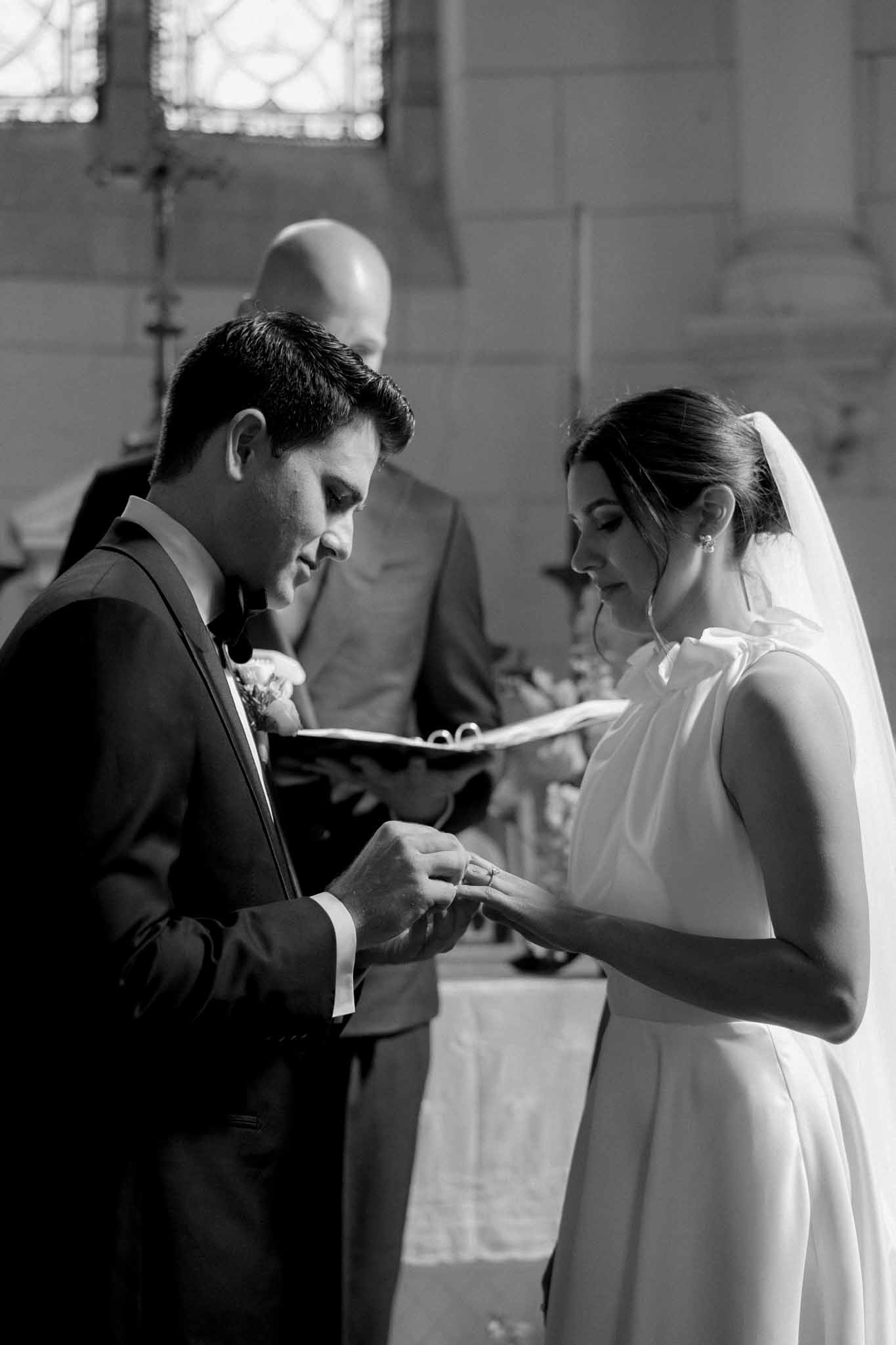 Black and white ring exchange, groom placing wedding band on bride's finger as she holds an open prayer book