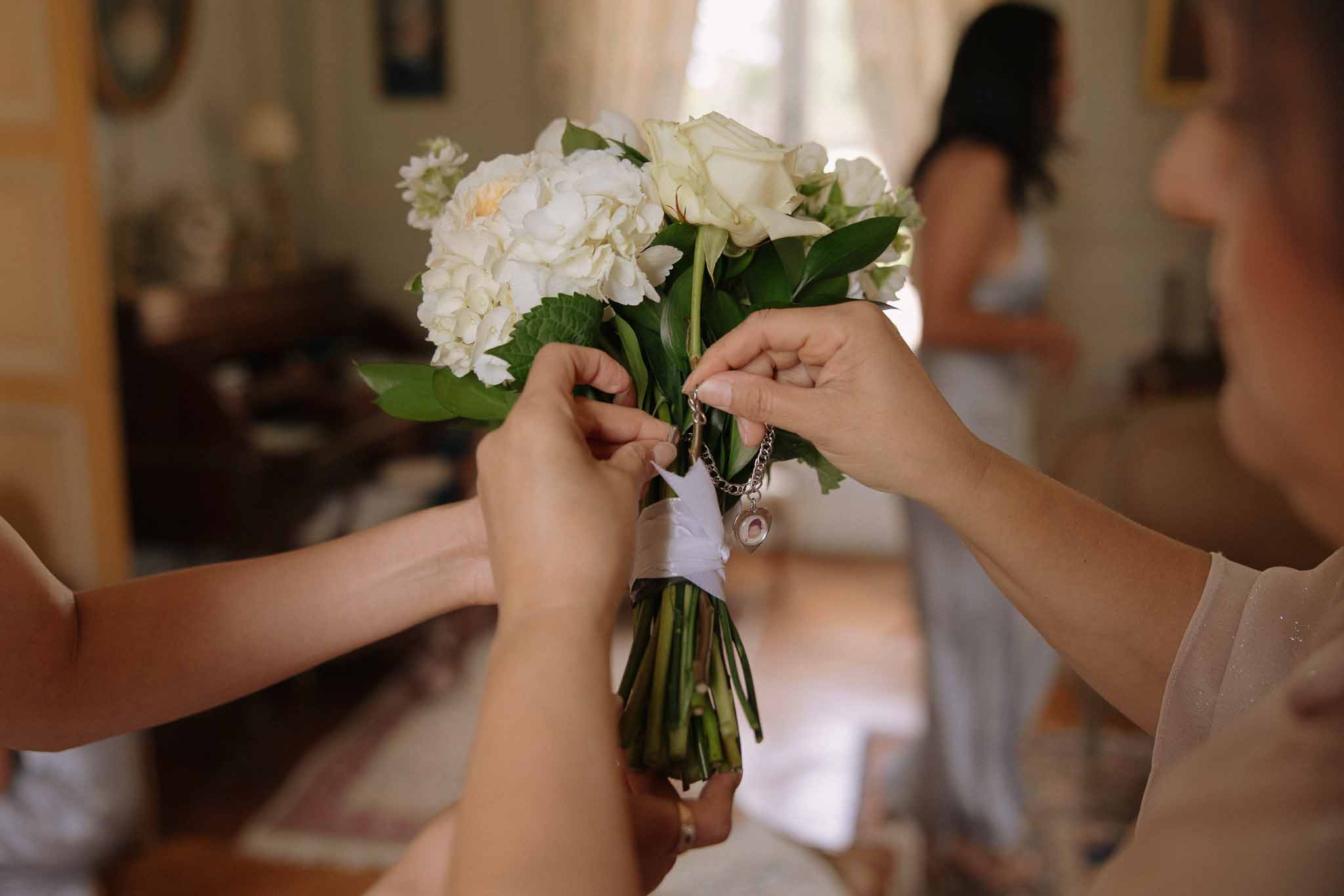 Close-up of bridal bouquet with ivory peonies and roses wrapped in white silk ribbon with a memorial locket
