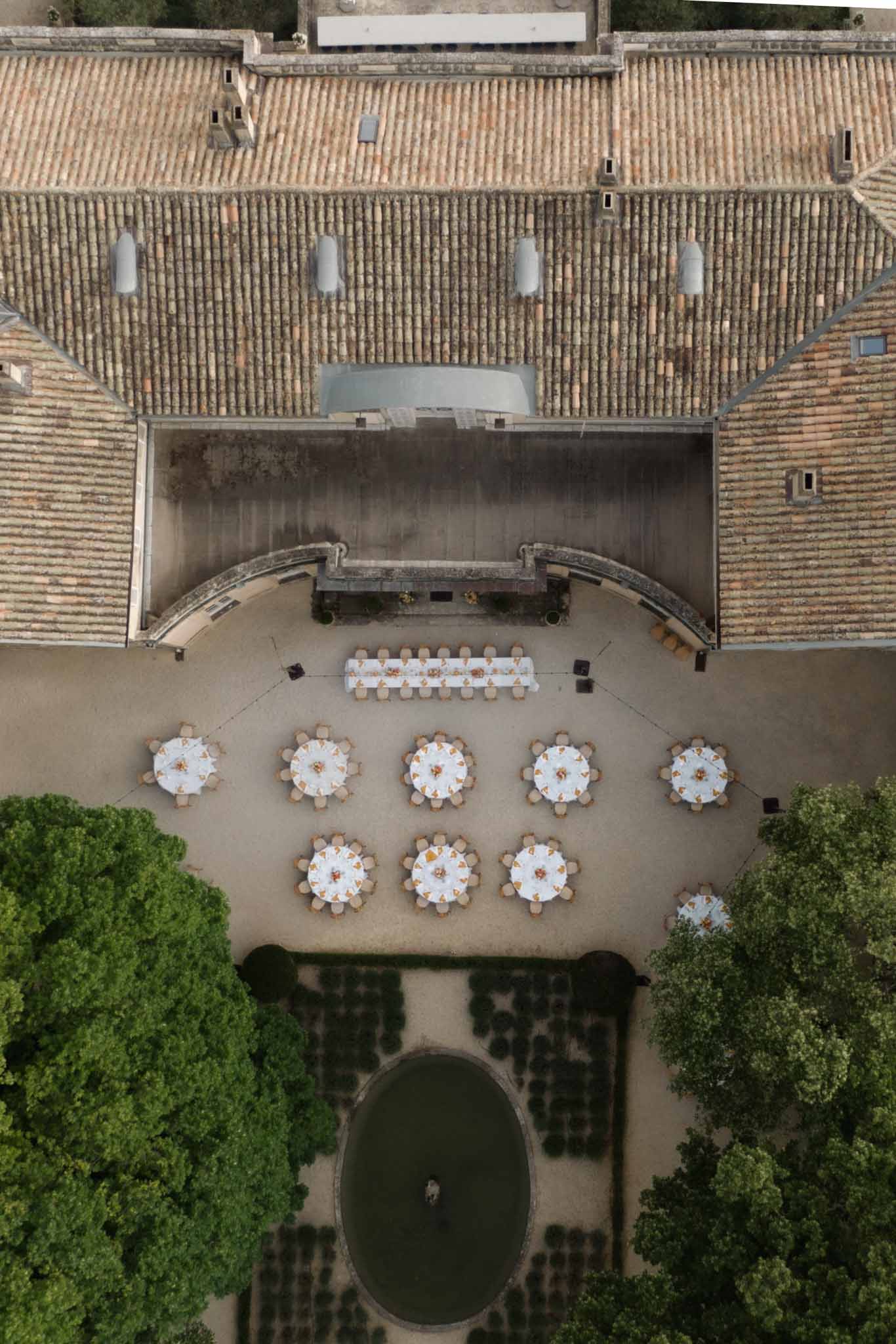 Aerial view of stone courtyard reception with white-linen round tables, terracotta tile roofs and manicured hedges